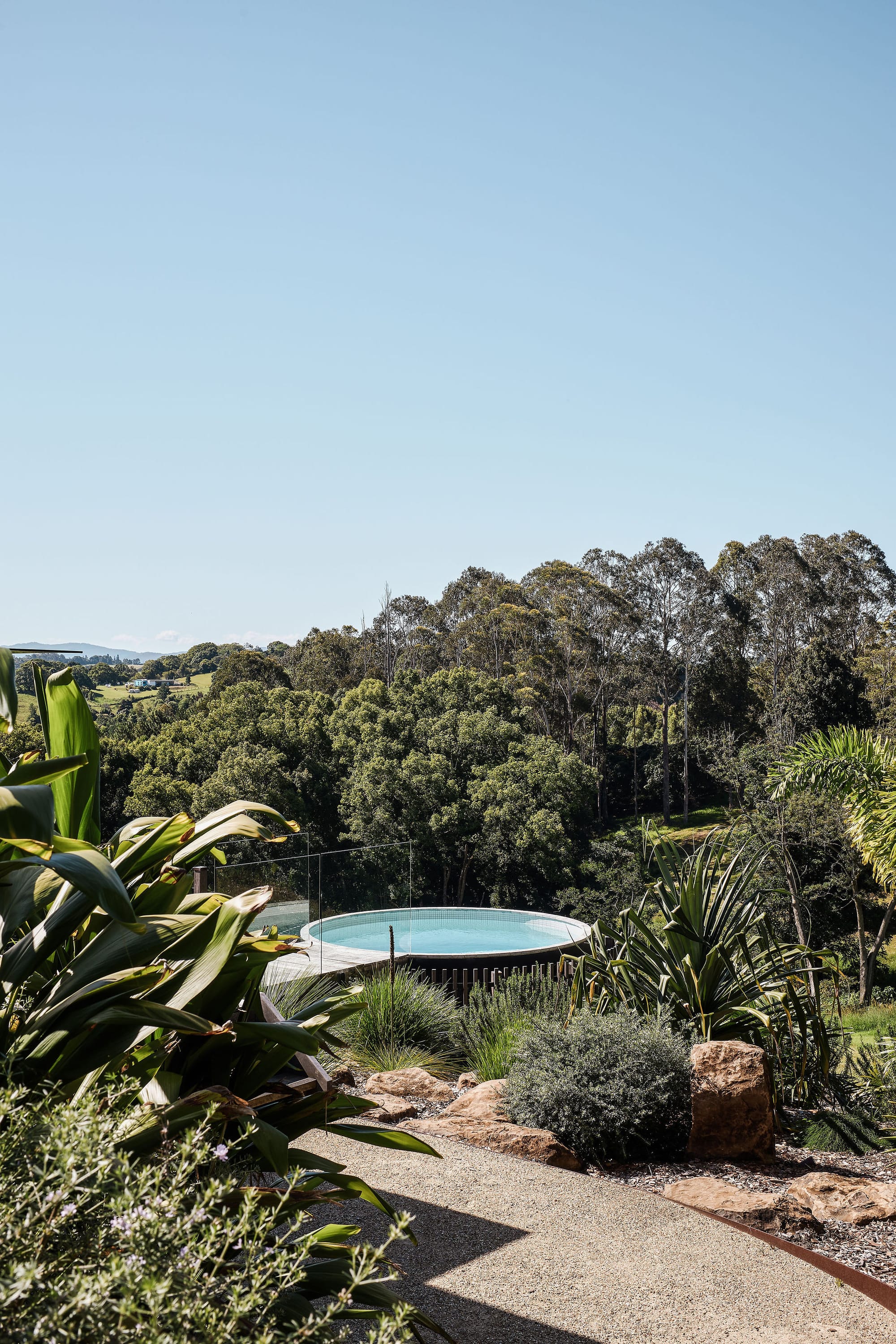 Rockpool Farm Byron Bay. Photography by Andy Macpherson. Round pool with timber walkway. Hillside views with lots of native plant life. Stone path.