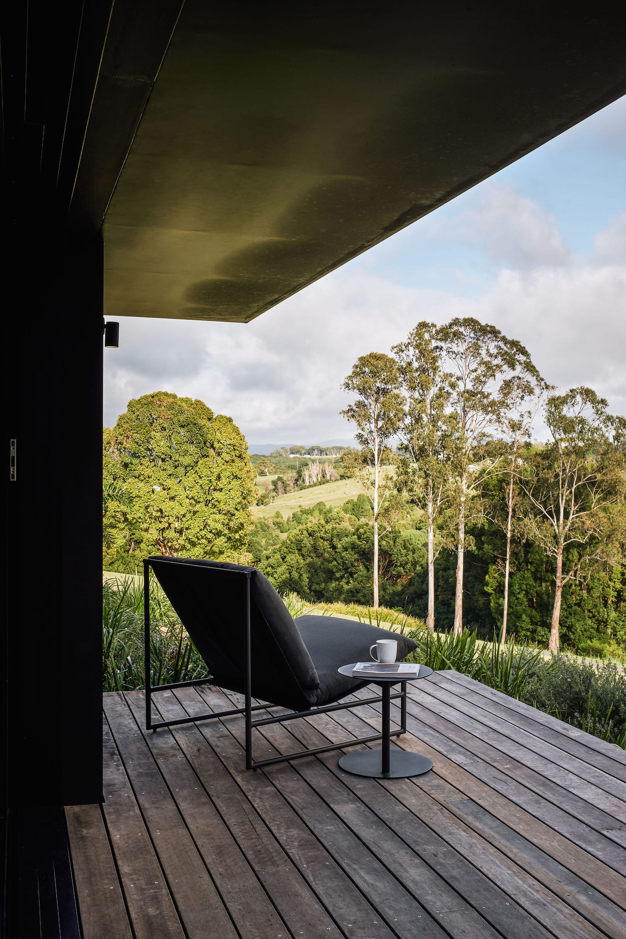 Rockpool Farm Byron Bay. Photography by Andy Macpherson. Outdoor chair sitting on timber deck, overlooking grassy hills and lush bush and trees.