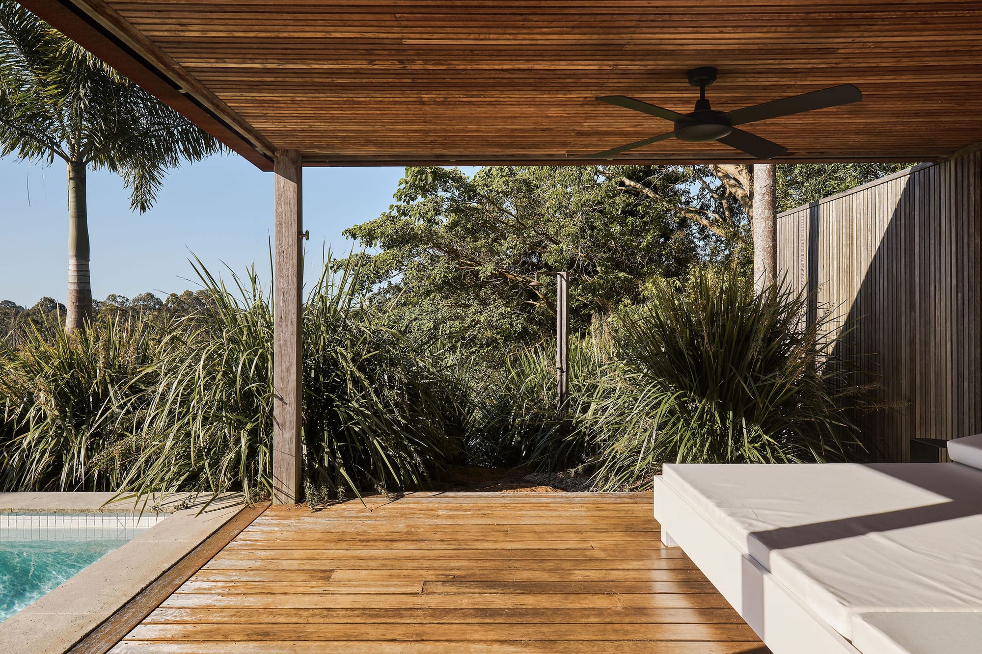 Rockpool Farm Byron Bay. Photography by Andy Macpherson. Timber deck alongside pool with white lounge beds. Timber clad ceiling. Surrounded by plants.