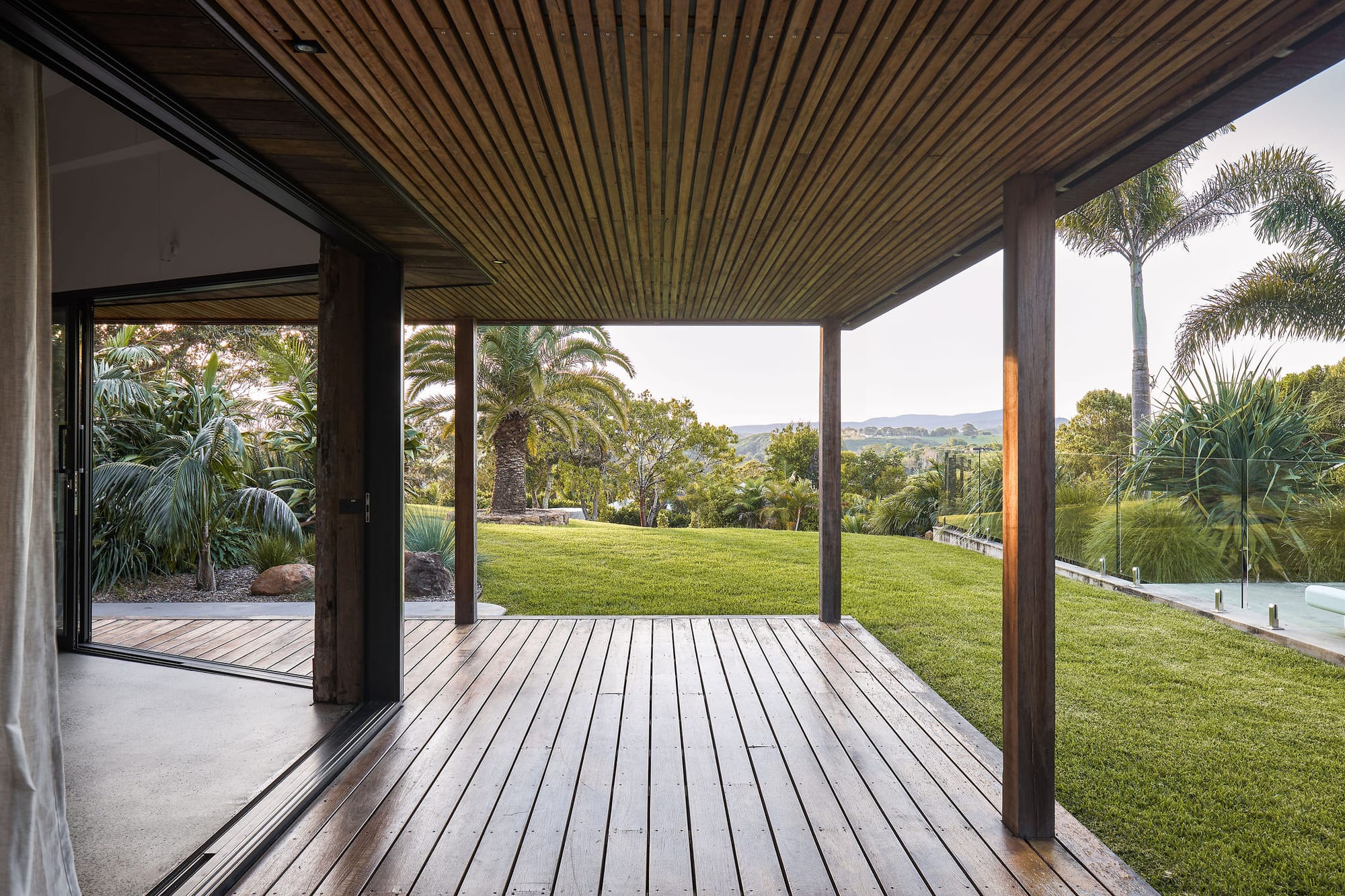 Rockpool Farm Byron Bay. Photography by Andy Macpherson. Timber wrap around deck with timber clad ceiling. Views over grassy hills, pool and lots of lush native plants.
