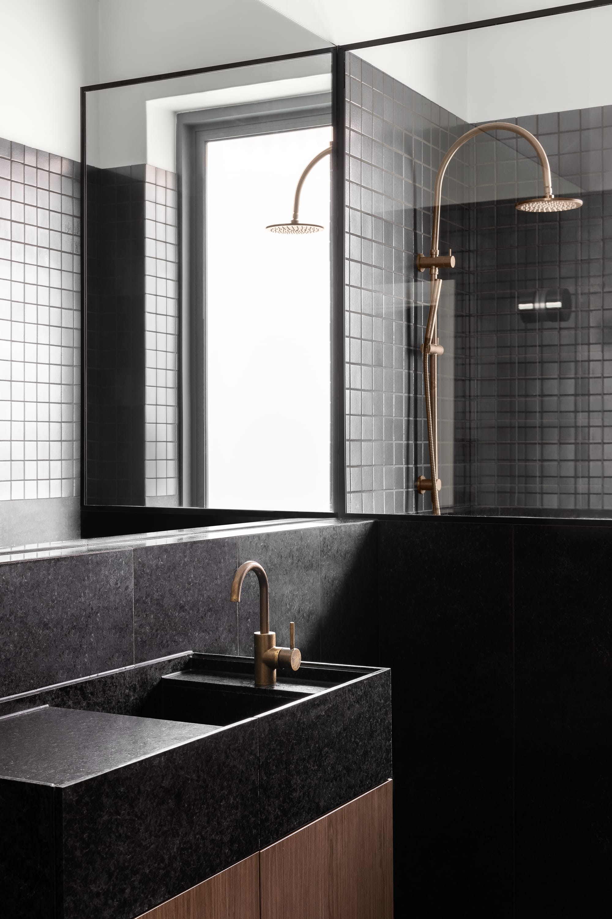 Rose Park by studio gram. Photography by Timothy Ross. Bathroom with black granite wall tiles, countertops and integrated sink. Wall mirror above sink. Bronze hardware. 