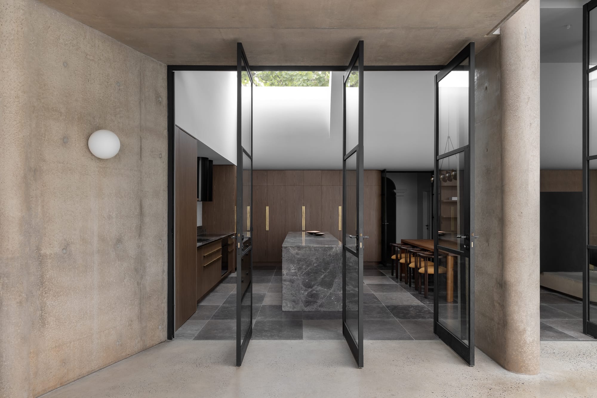 Rose Park by studio gram. Photography by Timothy Ross. Floor-to-ceiling spinning black-framed doors opening from outside area to kitchen. Concrete walls. 