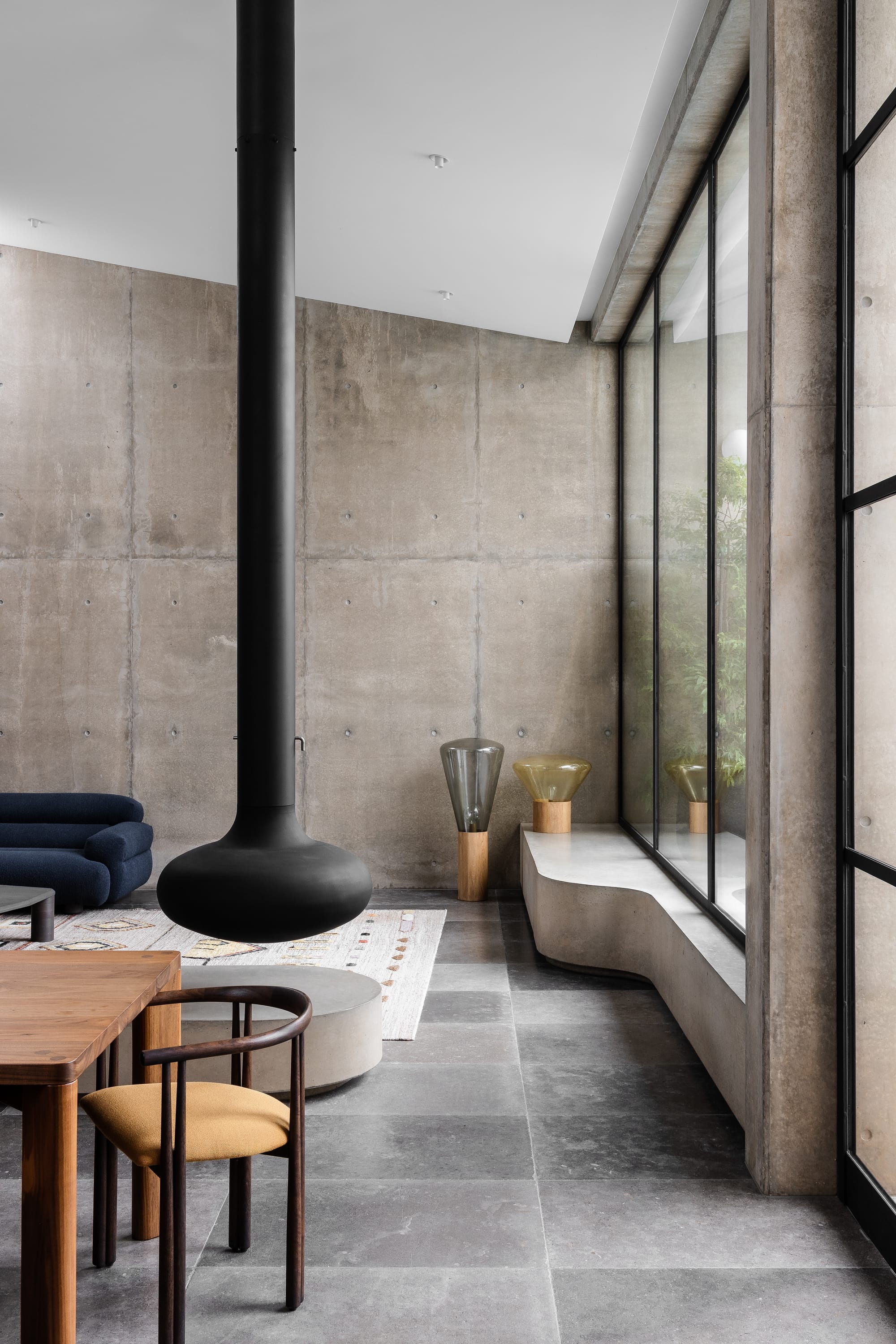 Rose Park by studio gram. Photography by Timothy Ross. Interior living space with tiled floors, concrete walls and black curved fireplace suspended from ceiling. Concrete bench runs along window. 