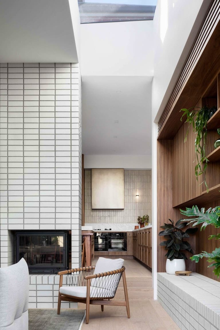 South Terrace Renovation by Chan Architecture. Photography by Tatjana Plitt. Sunken lounge with light timber floor and white brick fireplace. Mid-century modern timber kitchen in background. 