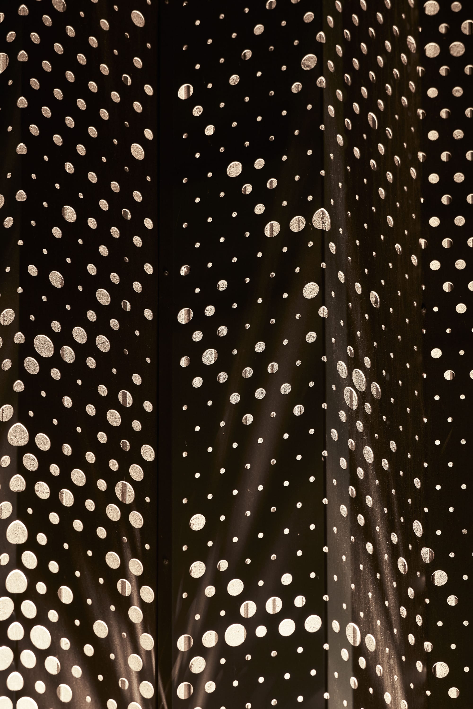 The Split Home by Seidler Group. Copyright of Seidler Group. Close up of perforated and pleated sheet of aluminum. Circles of varying sizes in metal. 