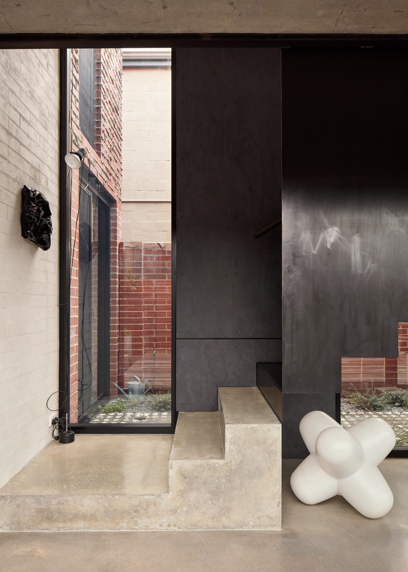Brick House by Studio Roam. Photography by Jack Lovel. Concrete and steel staircase. Polished concrete floors. Abstract white sculpture to right. 