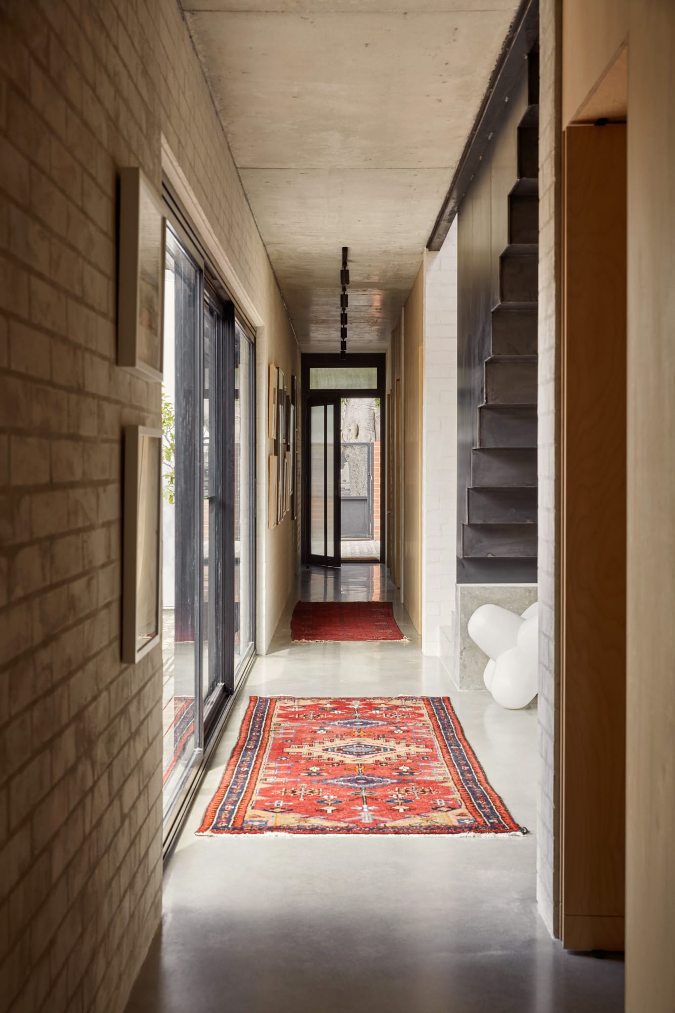 Brick House by Studio Roam. Photography by Jack Lovel. Polished concrete hallway with Aztec style rug.  Brick walls. 