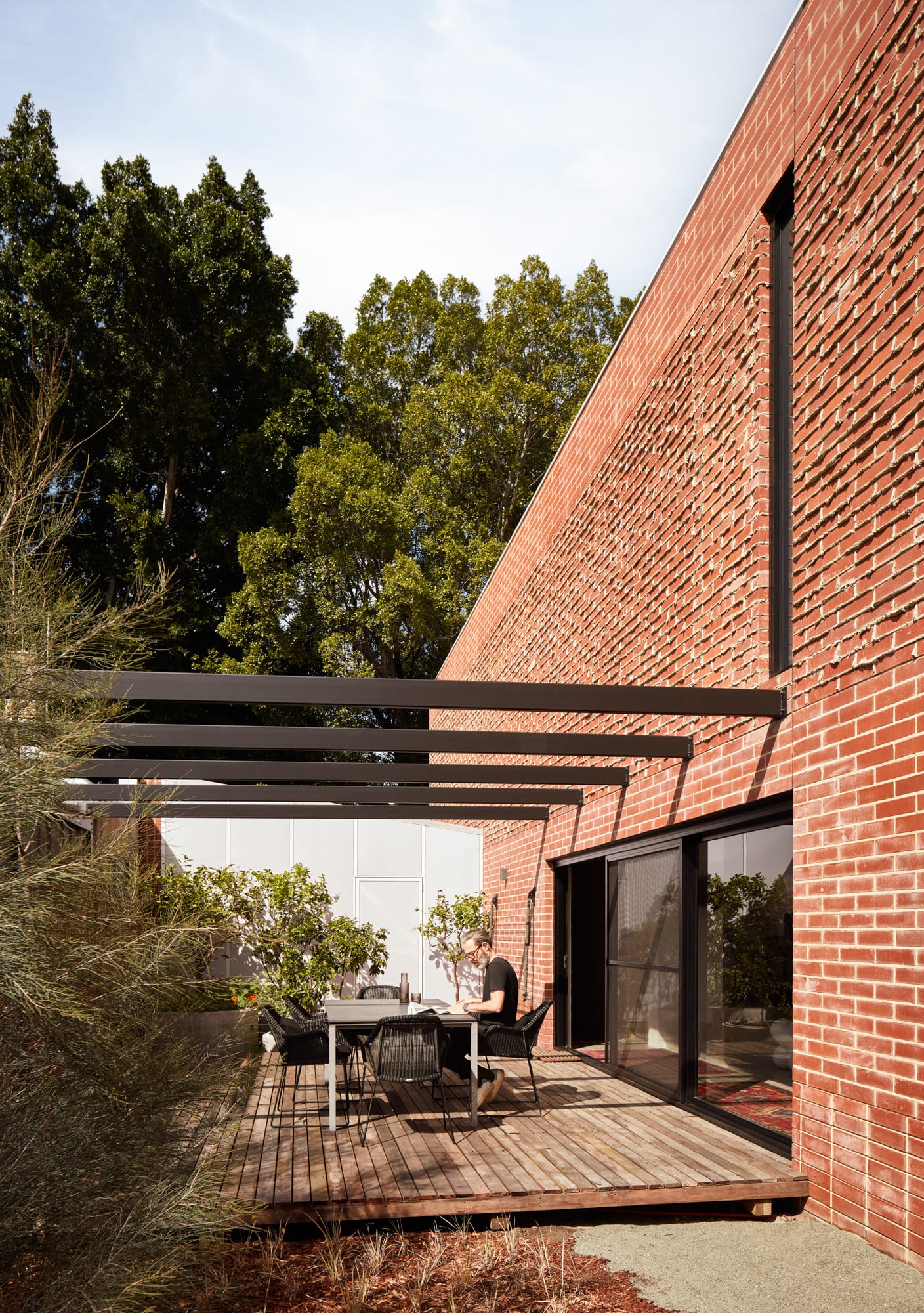 Brick House by Studio Roam. Photography by Jack Lovel. Outdoor courtyard and deck extending from ground floor of red brick home.