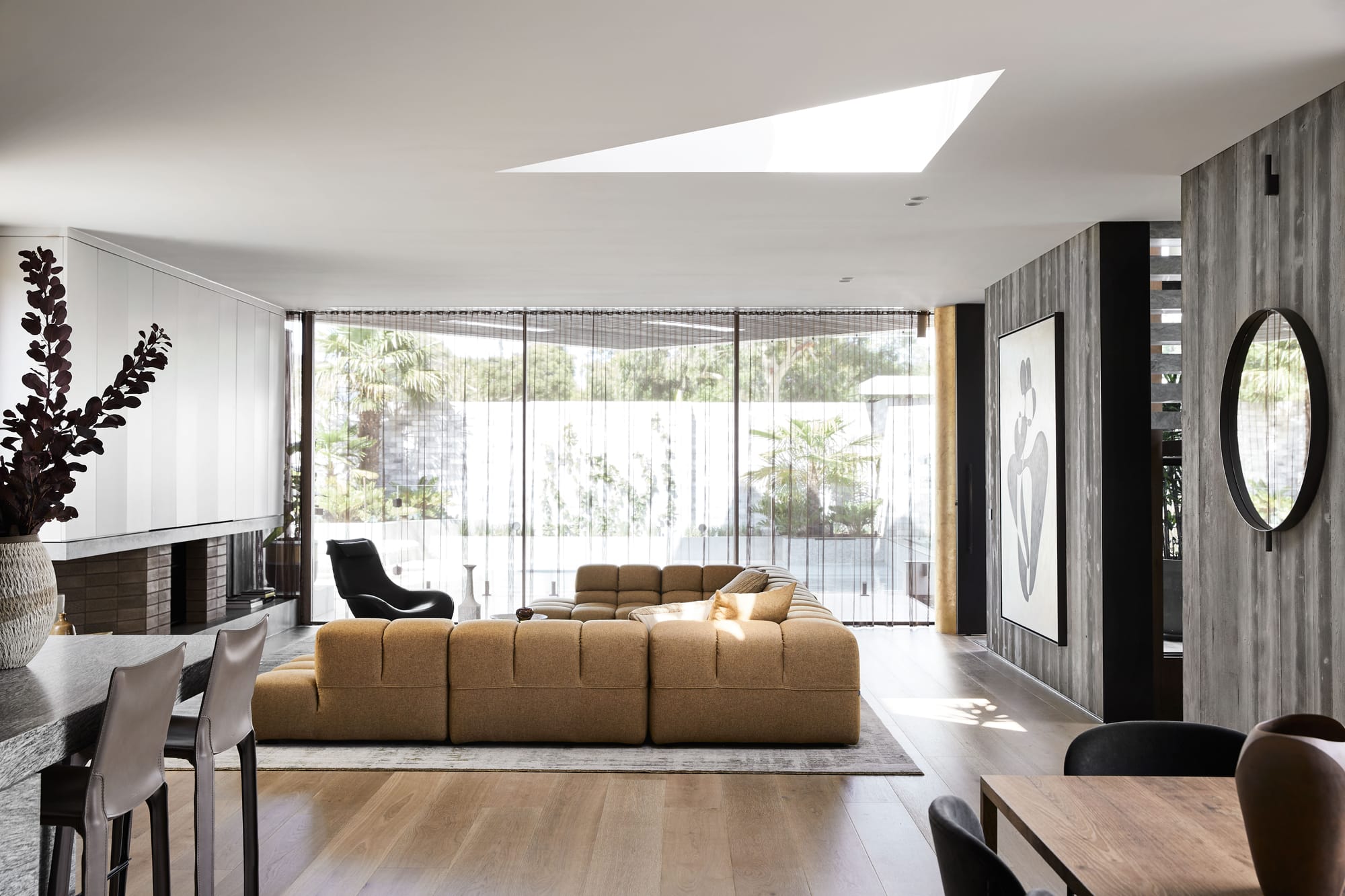 The Split Home by Seidler Group. Copyright of Seidler Group. Living room with floor-to-ceiling windows overlooking deck and pool outside. Black armchair and mustard couch inside. 