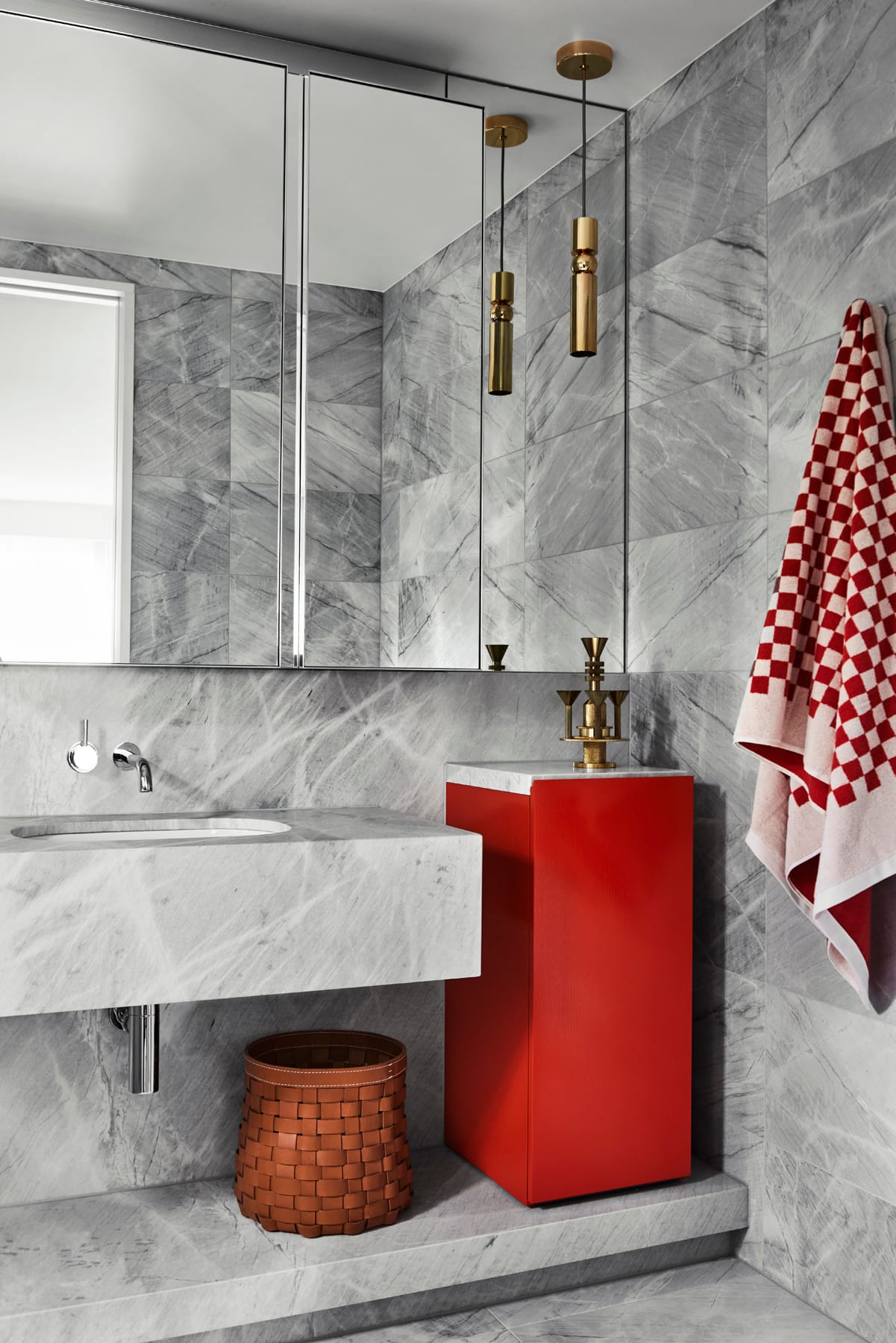 Toorak House 2 by K.P.D.O. Photography by Sharyn Cairns. Bathroom with grey stone floor, walls and basin. Bright red storage unit next to sink. Gold pendant lighting. 