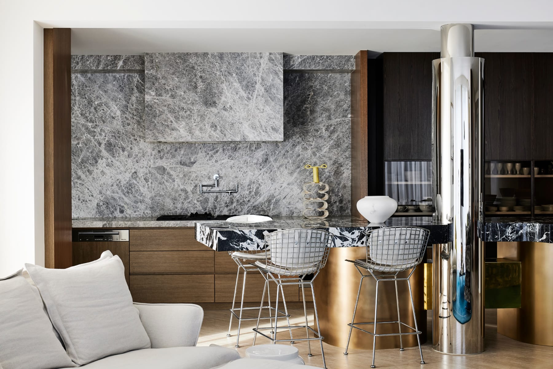 Toorak House 2 by K.P.D.O. Photography by Sharyn Cairns. Kitchen with grey stone splashback. Black and white stone countertops with bronze legs on island bench. Chrome pillar. 