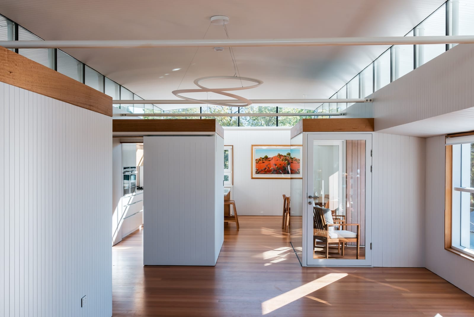 Wattle Bird House by Flett Architecture. Photography by Matt Sansom. Open plan kitchen and dining room with polished timber floors and white clad timber walls. High ceilings with windows around perimeter. 