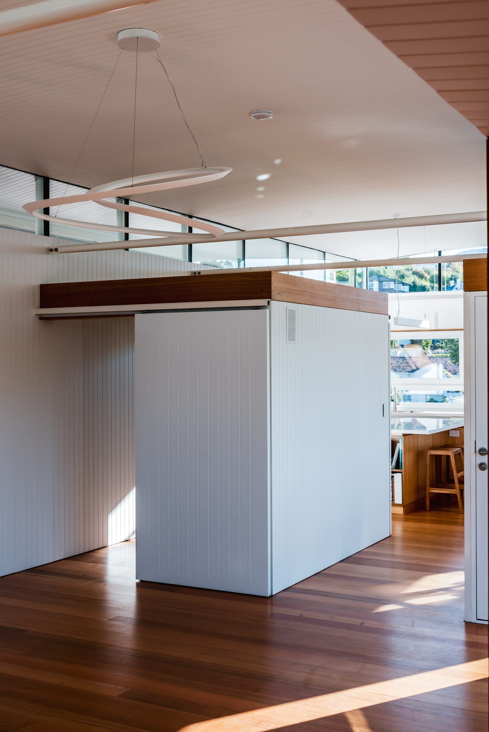 Wattle Bird House by Flett Architecture. Photography by Matt Sansom. White timber paneled walls dividing open plan dining space. Timber floors and high ceilings. 
