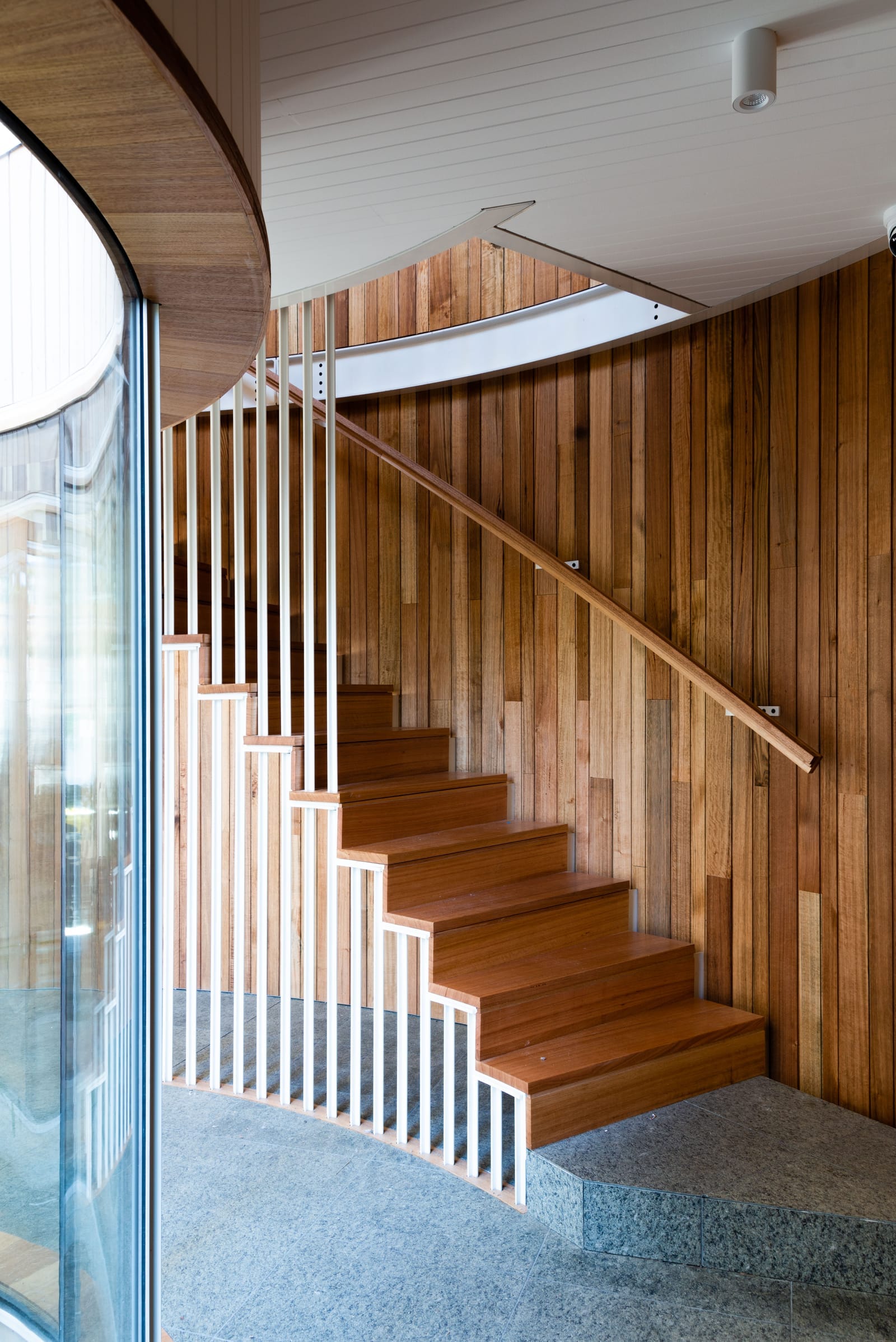 Wattle Bird House by Flett Architecture. Photography by Matt Sansom. Curved timber staircase with timber and metal balustrade. Timber clad walls. Stone tiled floors. 