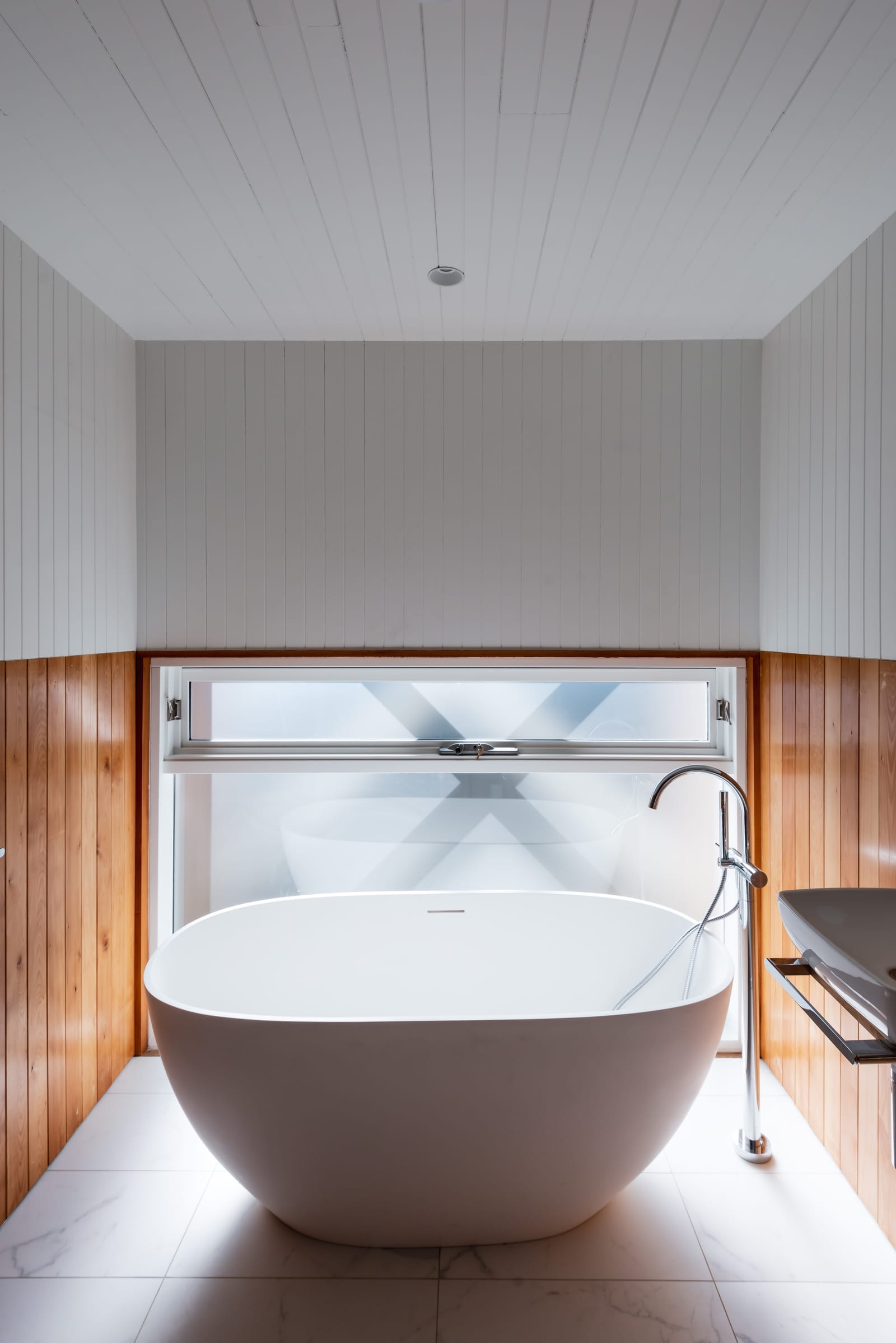Wattle Bird House by Flett Architecture. Photography by Matt Sansom. Round freestanding bath on white marble floor. Timber and white paneled walls.