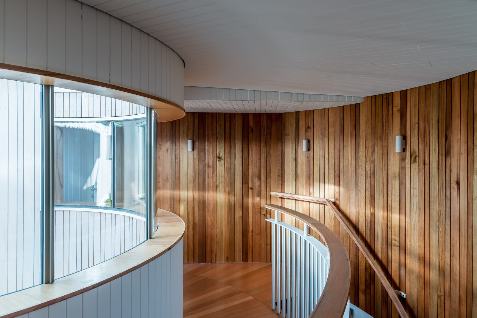 Wattle Bird House by Flett Architecture. Photography by Matt Sansom. Curved hallway and staircase with timber clad walls and ceiling. Timber balustrade and curved window.