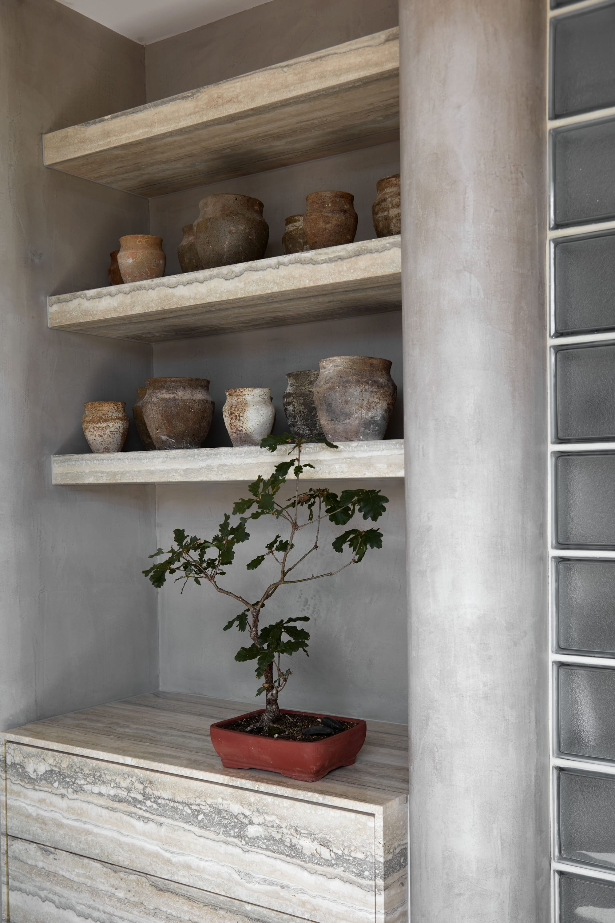 Zenn Showroom. Photography by Elisa Watson. Floor to ceiling shelving, storing cushions and vases. Concrete floors and walls. Glass block wall to left. 