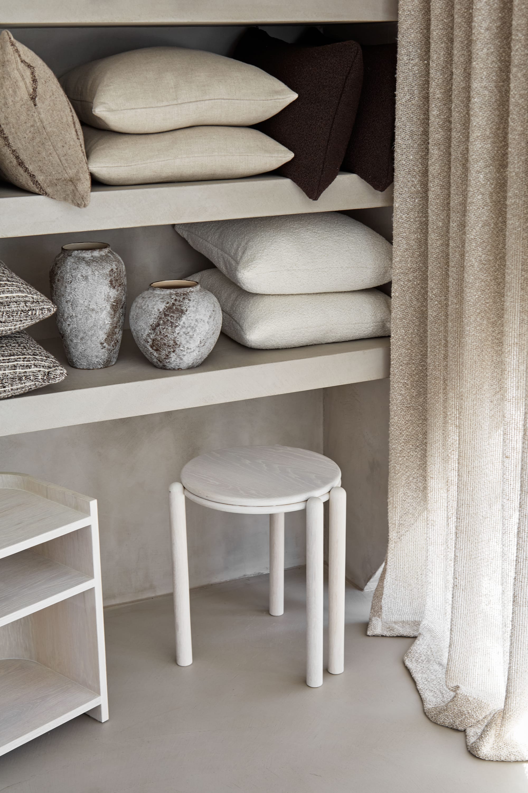 Zenn Showroom. Photography by Elisa Watson. White stool in front of plaster bookshelf, with vases and pillows on it. 