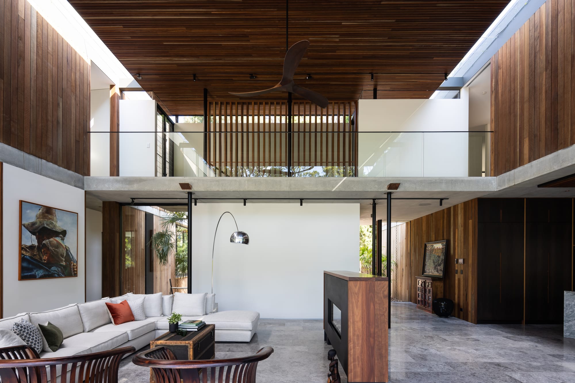 Mortlock Timbers Series: Fox Valley House. Photography by Simon Whitbread. Double height interior living space with stone floors and timber clad walls and ceiling. Concrete walkway on second level overlooks ground floor living space. 