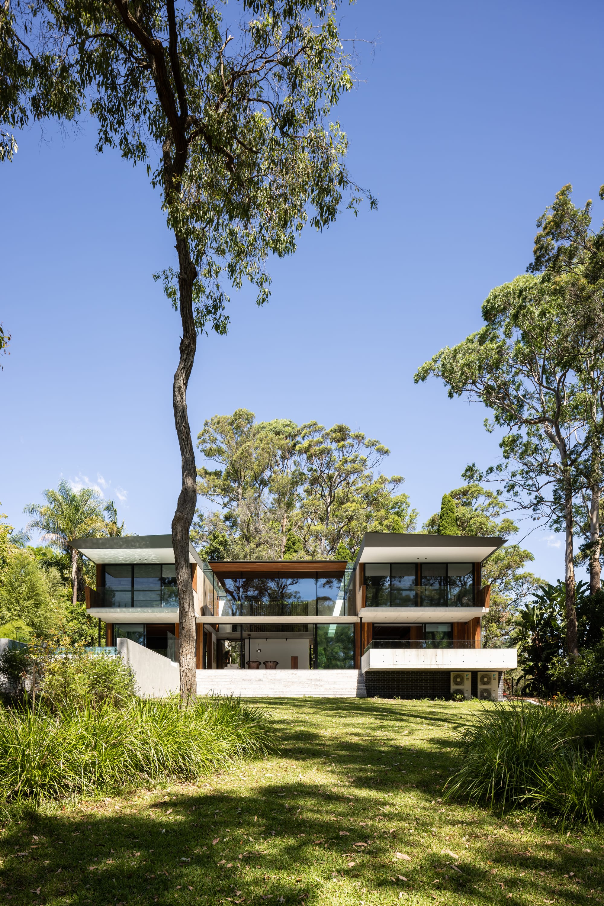 Mortlock Timbers Series: Fox Valley House. Photography by Simon Whitbread. Rear facade of double storey home with symmetrical wings. Green and grassy native plants in backyard. 