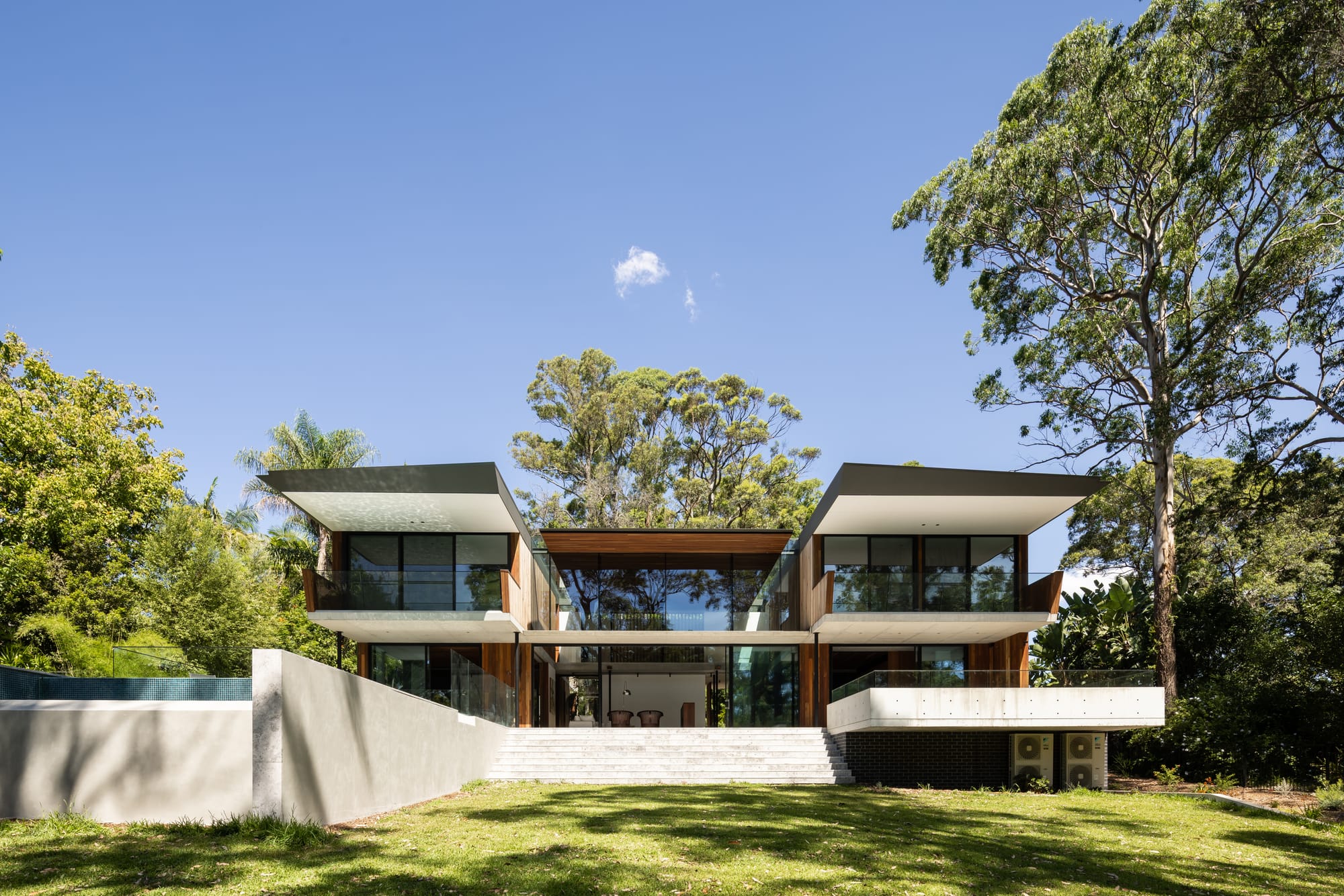 Mortlock Timbers Series: Fox Valley House. Photography by Simon Whitbread. Rear facade of double storey residential home with two sings and infinity pool to the left. Grassy backyard. 
