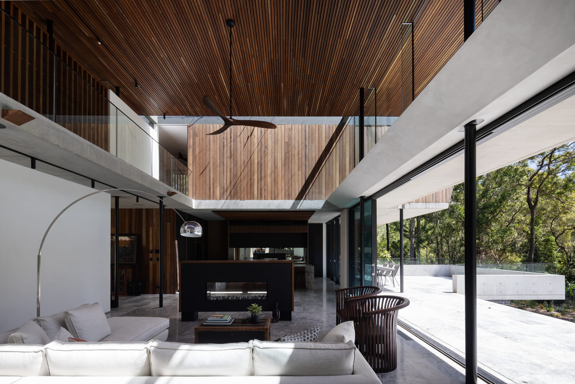 Mortlock Timbers Series: Fox Valley House. Photography by Simon Whitbread. Double height interior living space with floor-to-ceiling windows overlooking patio. Timber clad ceiling and walls. Overhead walkway. 