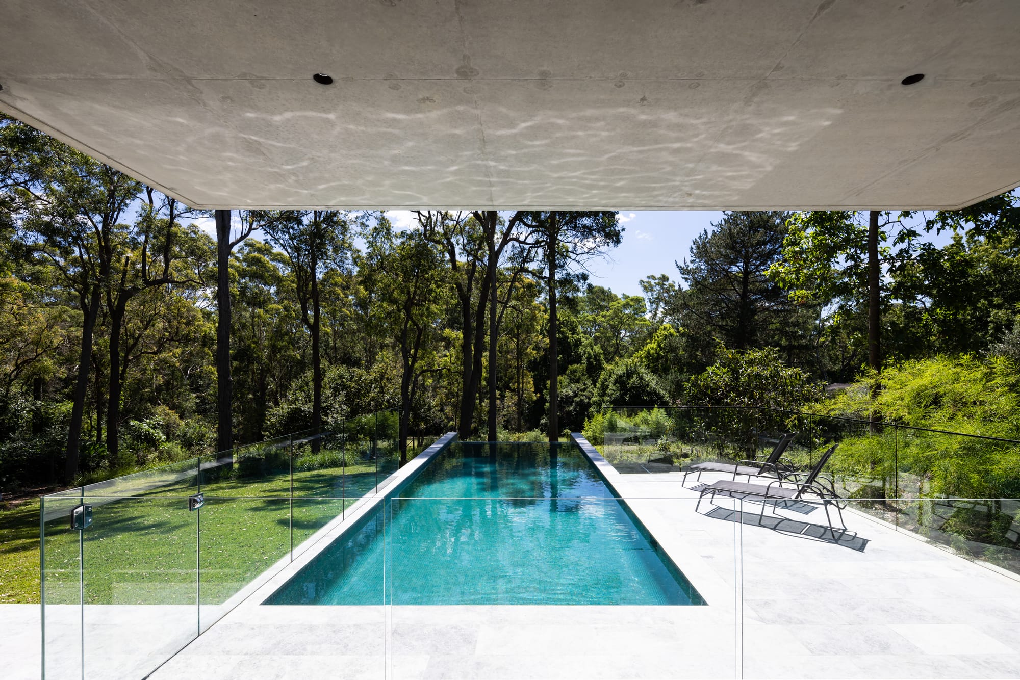 Mortlock Timbers Series: Fox Valley House. Photography by Simon Whitbread. Infinity pool extending from concrete verandah and patio out over grassy backyard. Partial shade from overhead concrete outcropping. 