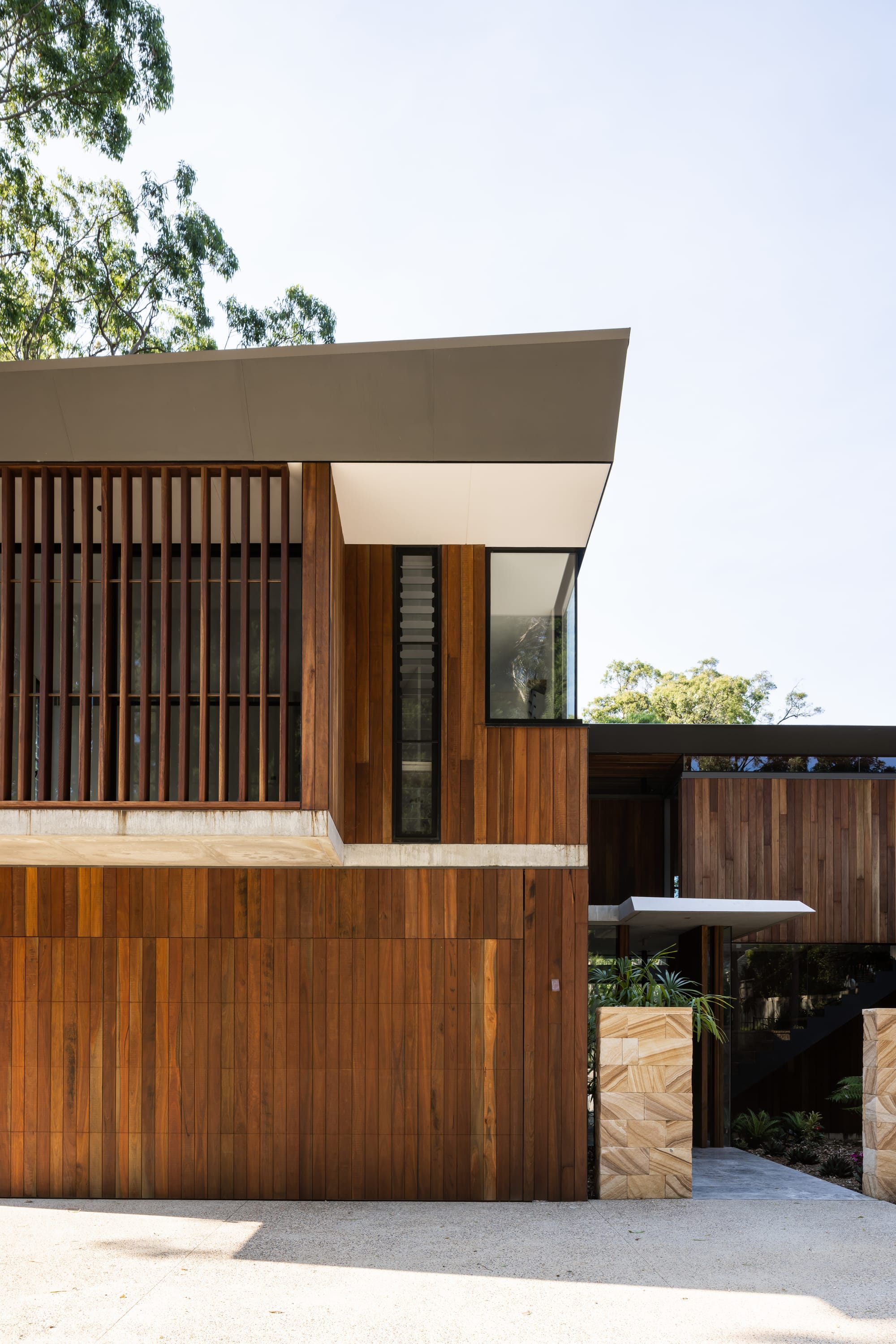 Mortlock Timbers Series: Fox Valley House. Photography by Simon Whitbread. Timber clad facade of double storey residential home. Angular roof, stone pillars by front entrance.