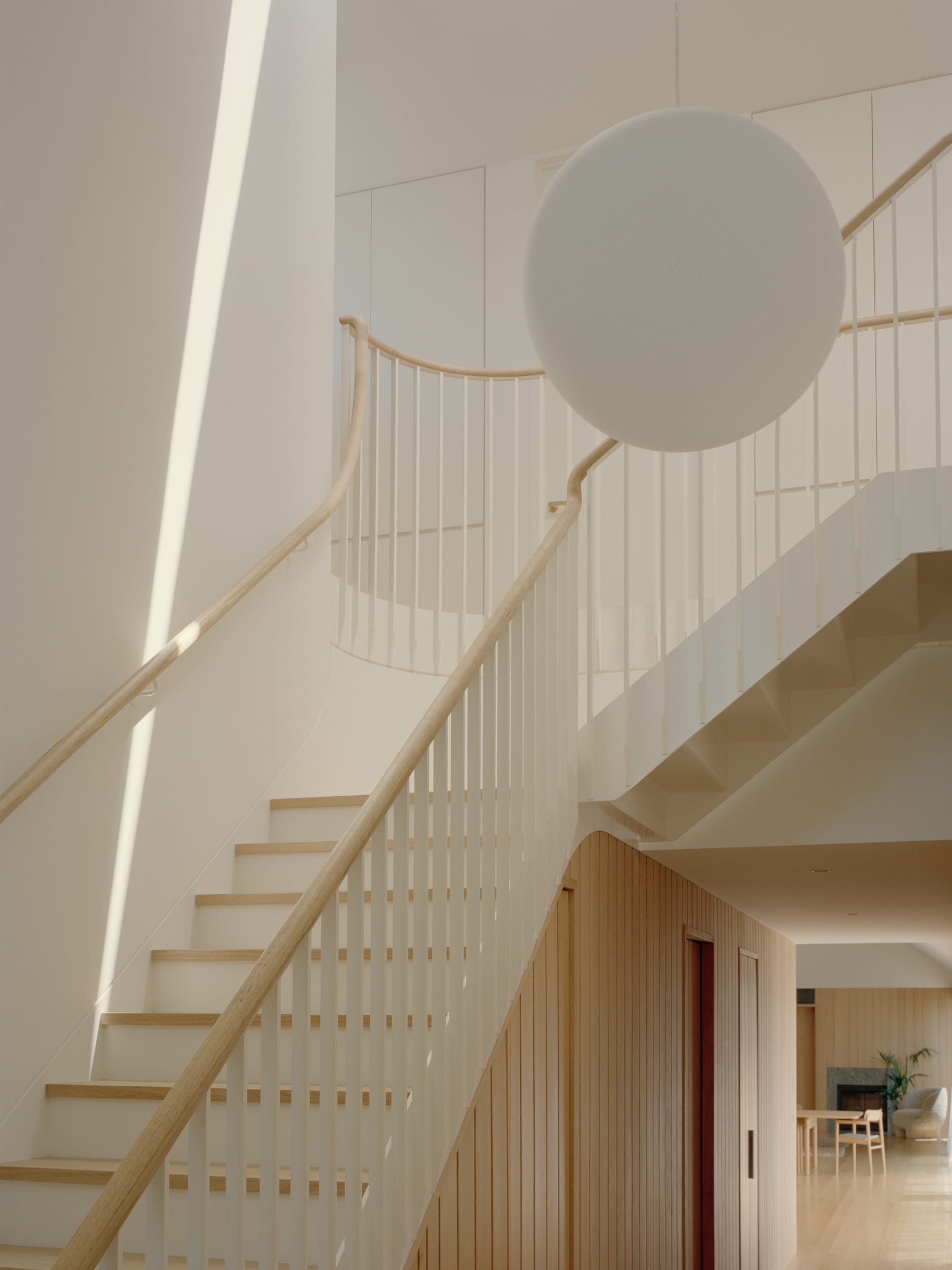 Gable Park by Weaver+Co Architects. Photography by Tasha Tylee. Timber and white staircase in residential home with large void. Spherical pendant hangs in void. Side of stairs clad in light timber. 