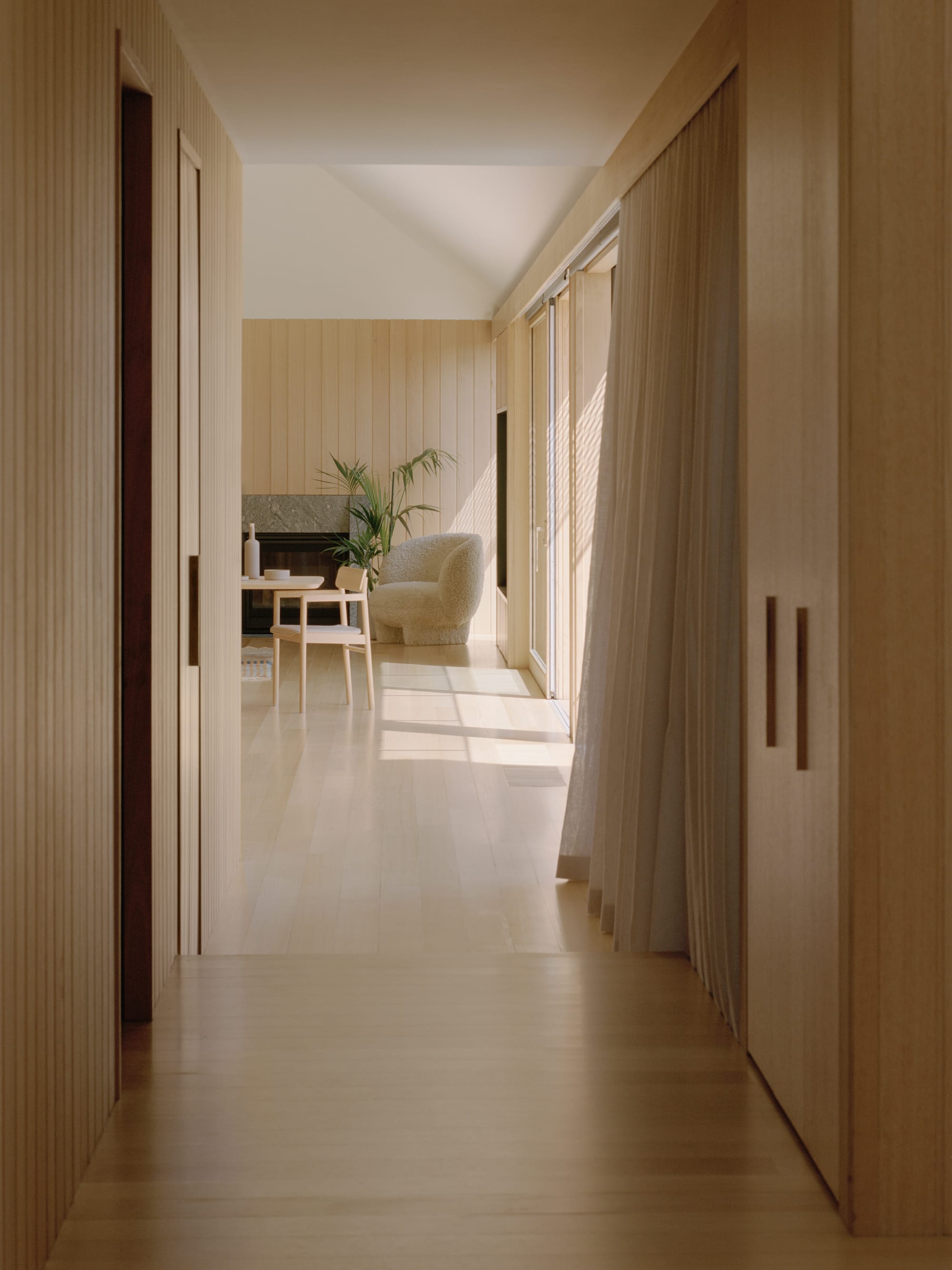 Gable Park by Weaver+Co Architects. Photography by Tasha Tylee. Hallway with timber walls and floors opens onto open plan dining and living room. High white cathedral ceilings and sliding doors let in light. 