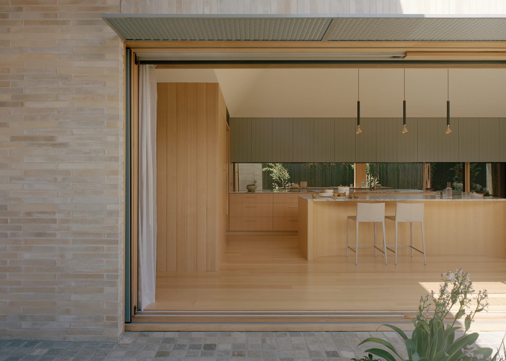 Gable Park by Weaver+Co Architects. Photography by Tasha Tylee. View from enclosed courtyard into kitchen in residential home. Timber floors, walls and cabinetry. Light brick wall exterior.