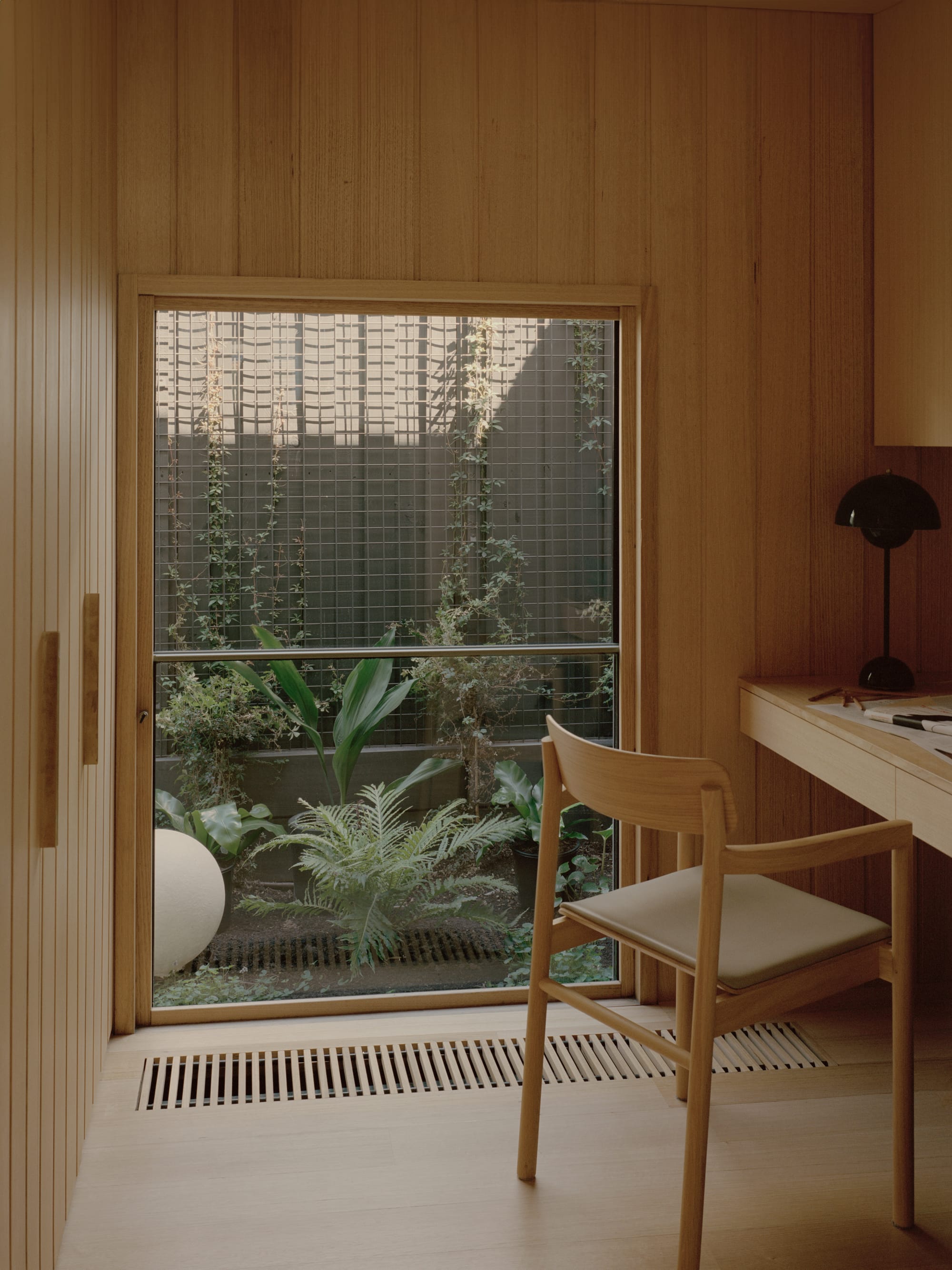 Gable Park by Weaver+Co Architects. Photography by Tasha Tylee. Study in residential home with timber clad walls and floors. Integrated timber desk with mid-century modern timber chair. Window looks onto lush courtyard garden.