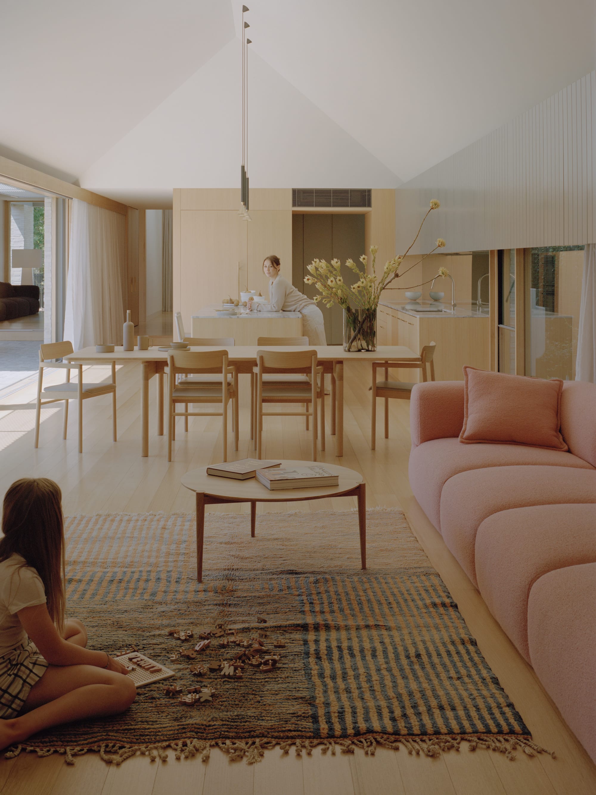 Gable Park by Weaver+Co Architects. Photography by Tasha Tylee. Open plan kitchen, living and dining space with timber floors, walls, cabinetry and dining setting. Pink boucle lounge. High, white cathedral ceilings.  