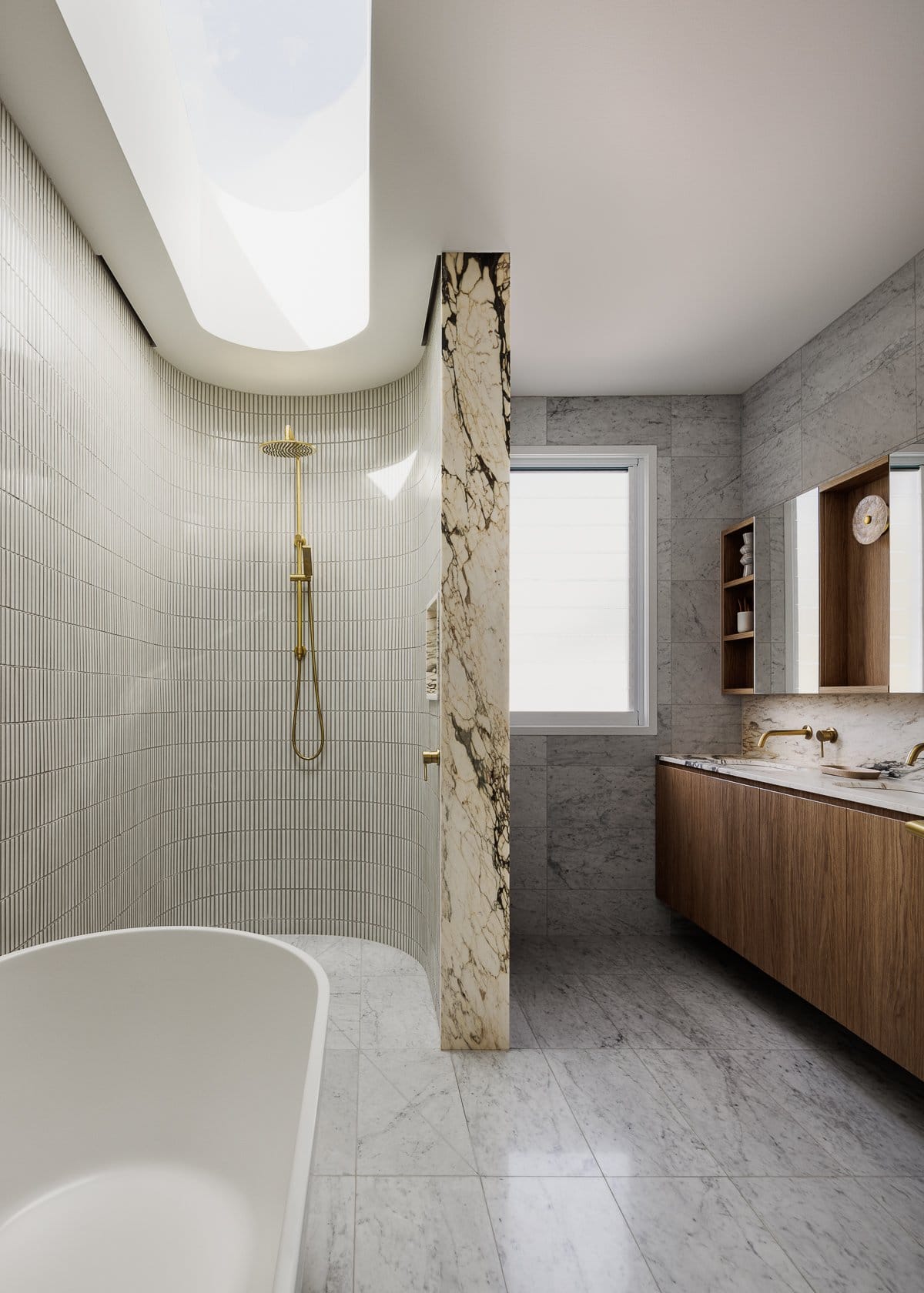 Hazlewood House by Favell Architects. Photography by Andy Macpherson. Bathroom with finger tiled curved shower. Marble feature wall. Stone tiles floors and splashback with timber cabinets. 