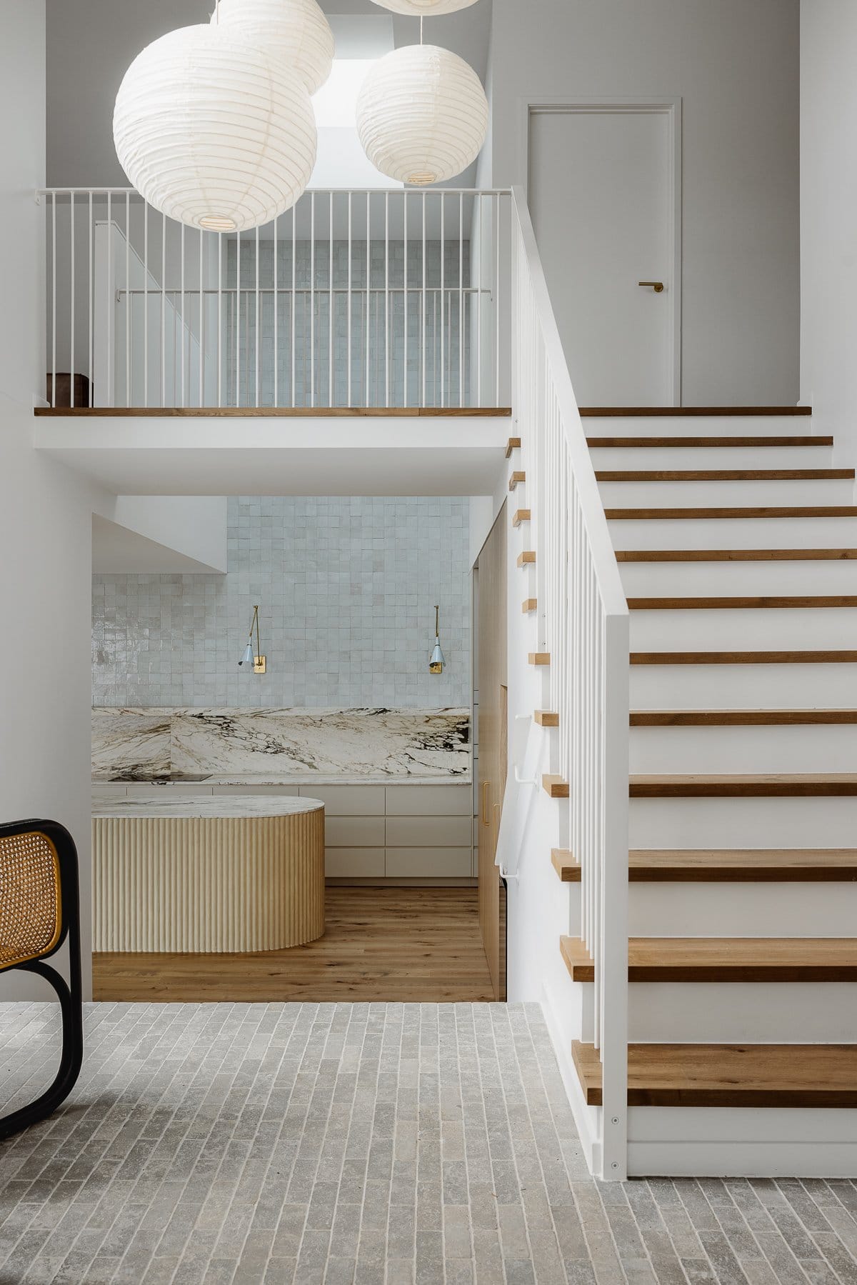 Hazlewood House by Favell Architects. Photography by Andy Macpherson. Grey tiled entryway to home with white and timber staircase leading upstairs. Stairs at end of hallway leading to kitchen, with timber floors and marble splashback.