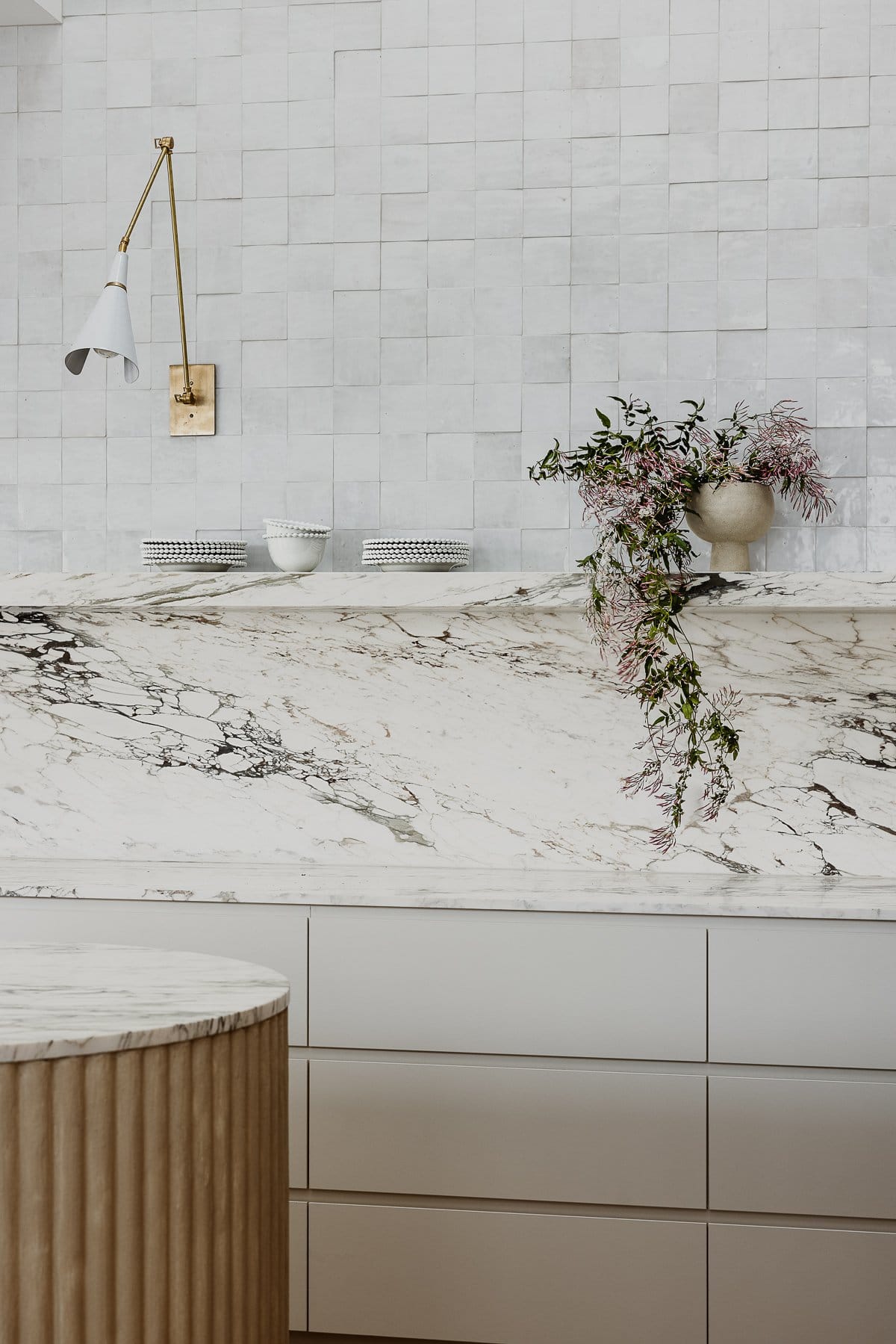 Hazlewood House by Favell Architects. Photography by Andy Macpherson. Kitchen with fluted timber and white marble island bench. White cabinets with white marble countertops and splashback. Marble shelf and white tiles.