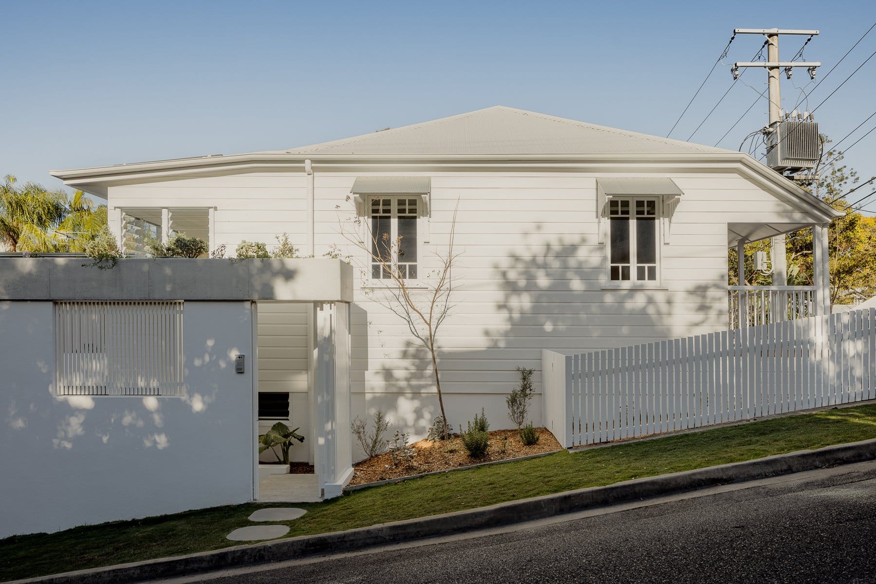 Hazlewood House by Favell Architects. Photography by Andy Macpherson. Side street facade of white clad cottage. Steep hill street access. White picket fence. 