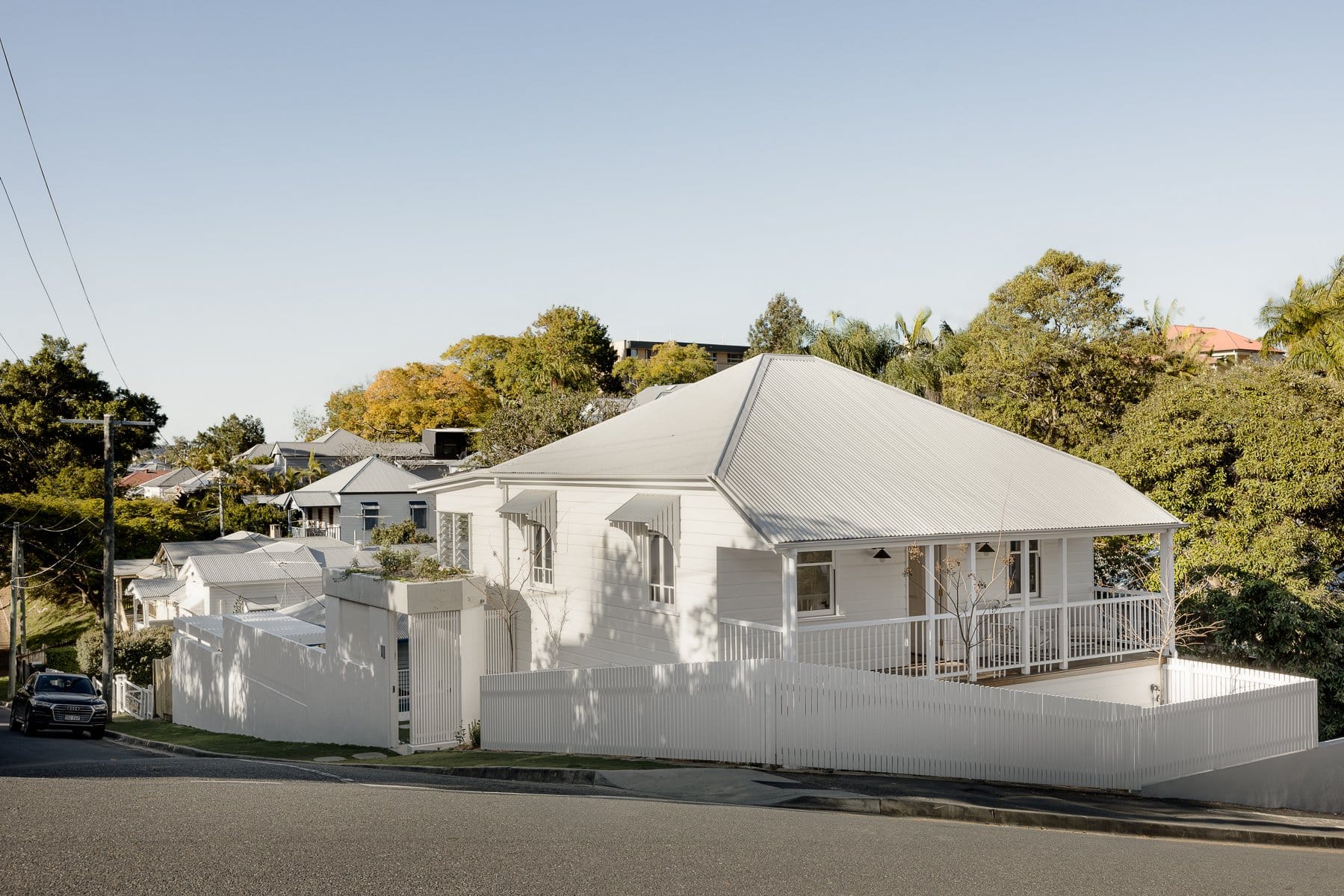 Hazlewood House by Favell Architects. Photography by Andy Macpherson. White clad renovated cottage home on corner hillside lot. White picket fence around entire home.