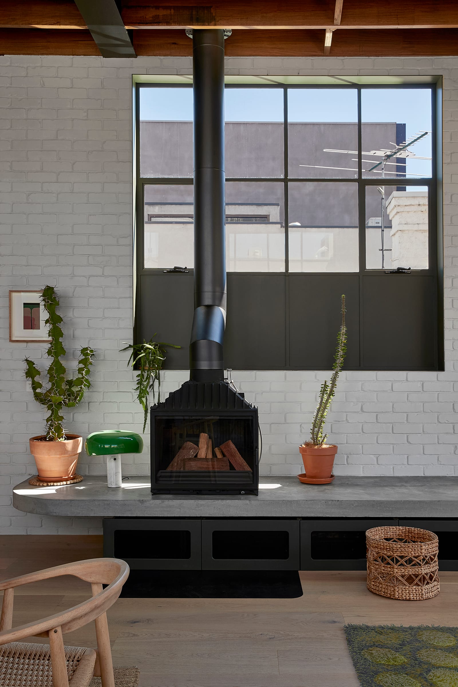 Fabrica by mcmahon and nerlich. Photography by Shannon McGrath. Black metal fireplace on floating concrete bench in front of white brick wall. Timber floors. Black metal grid framed window.