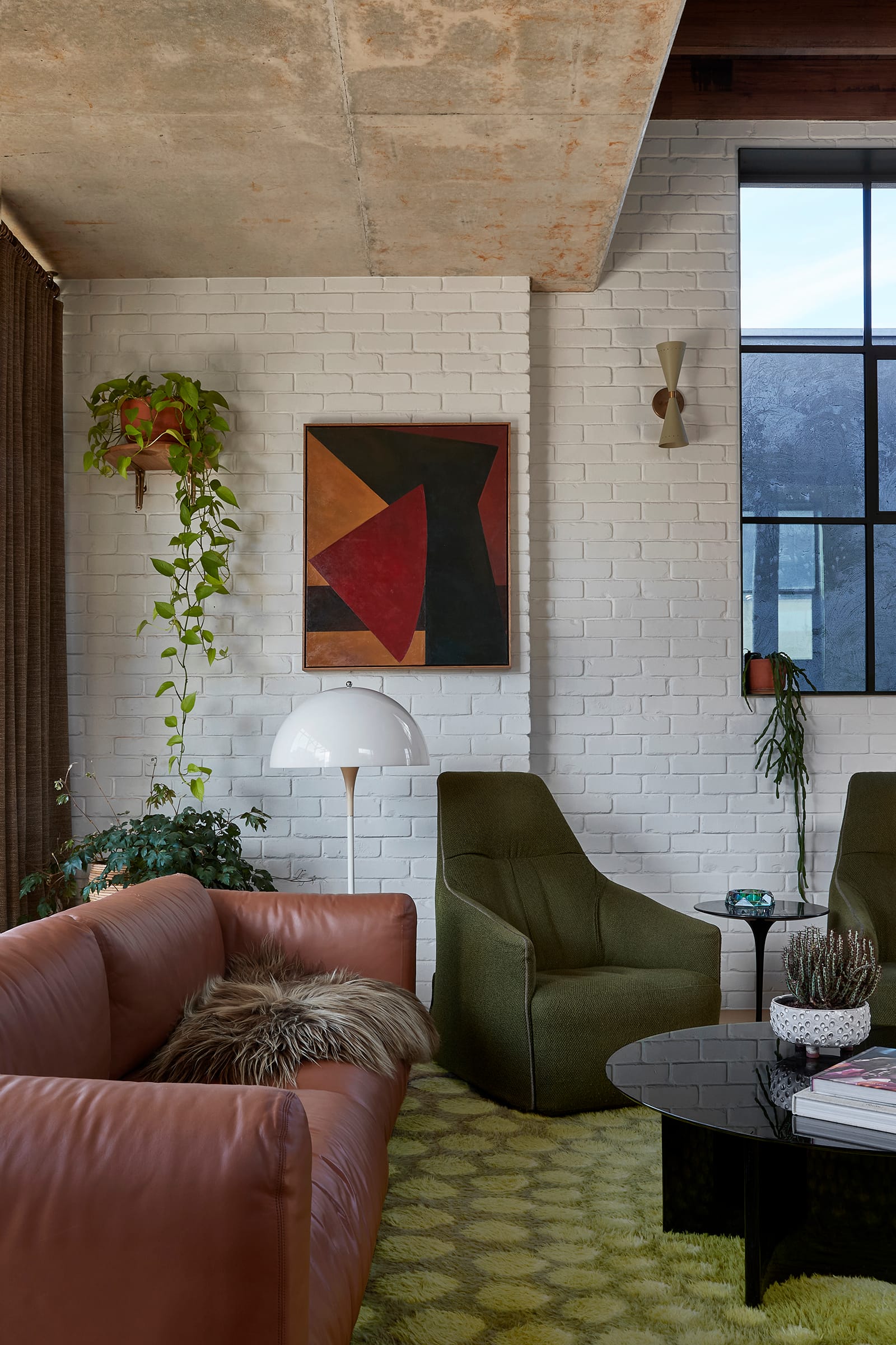Fabrica by mcmahon and nerlich. Photography by Shannon McGrath. Living space with green rug, green armchairs and brown leather couch. Eclectic furnishings. White brick wall.