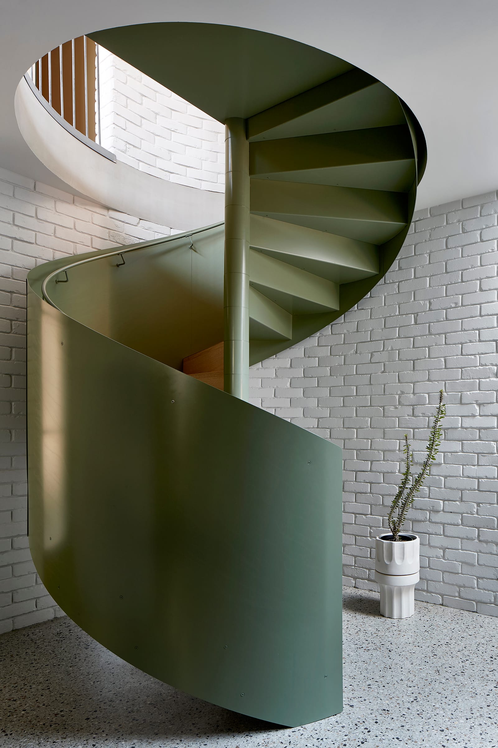 Fabrica by mcmahon and nerlich. Photography by Shannon McGrath. Green metal spiral staircase with green railing. Terrazzo floor and white brick walls. 