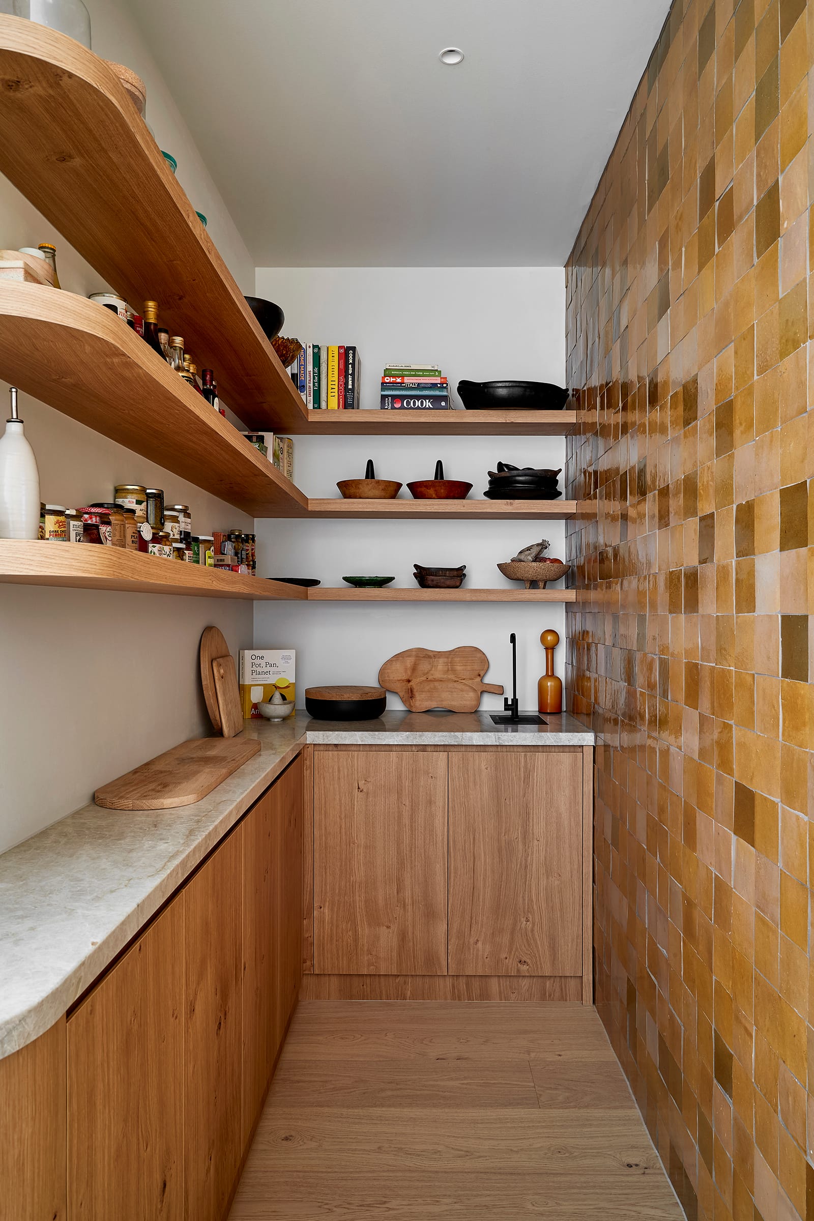 Fabrica by mcmahon and nerlich. Photography by Shannon McGrath. Scullery kitchen with timber cabinetry and stone benchtop. Beige tiled wall. Timber floors and floating timber shelves.