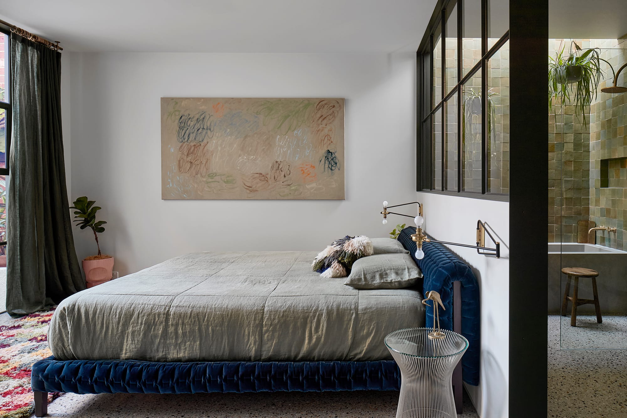 Fabrica by mcmahon and nerlich. Photography by Shannon McGrath. Master bedroom with blue velet bedframe and white walls. Windowed wall looking onto ensuite with green wall tiles and hanging plants. 