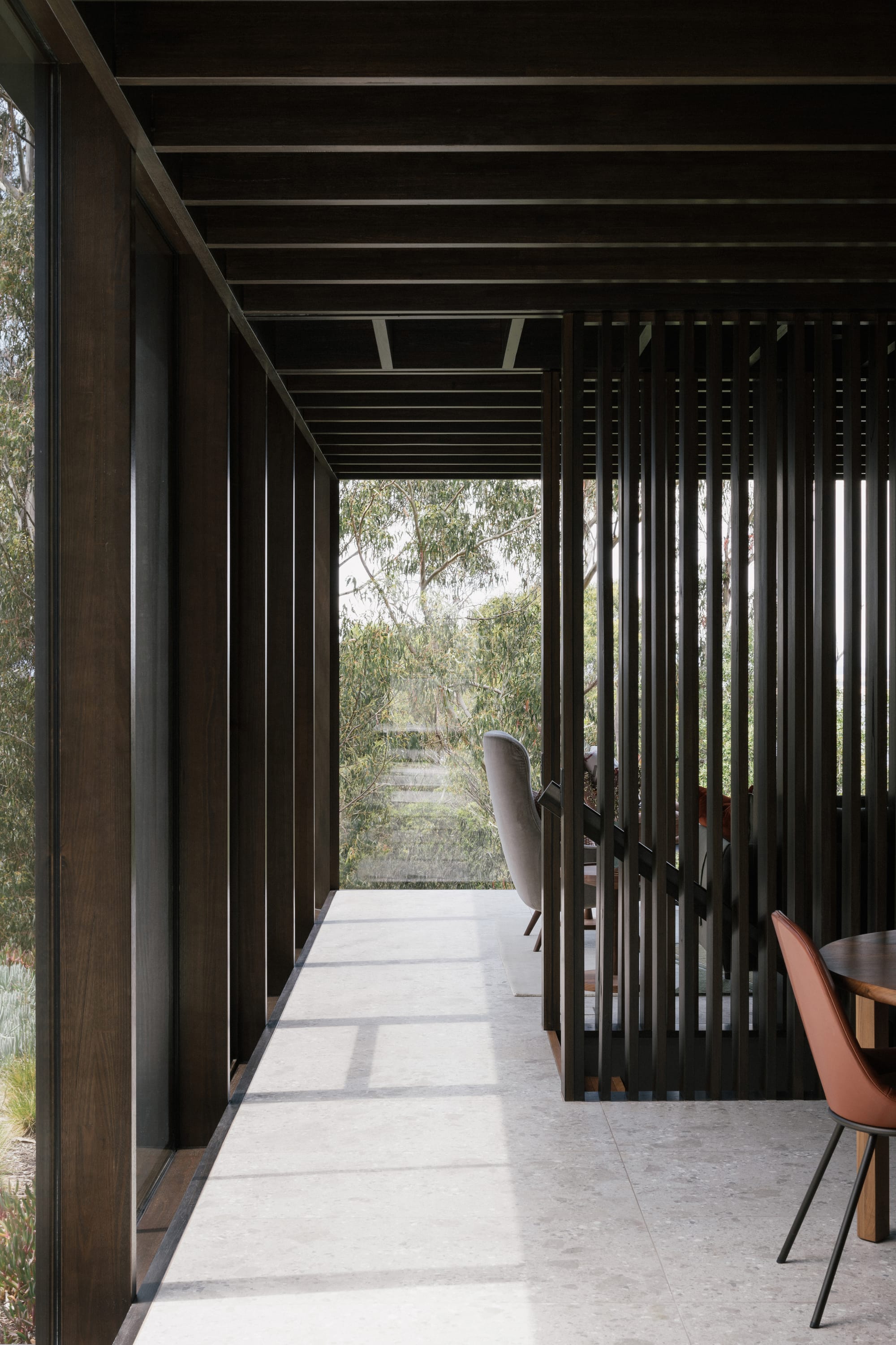 Taroona House by Archier. Photography by Thurston Empson. Stone floor on second level of residential home. Timber framed windows overlooking native busland.