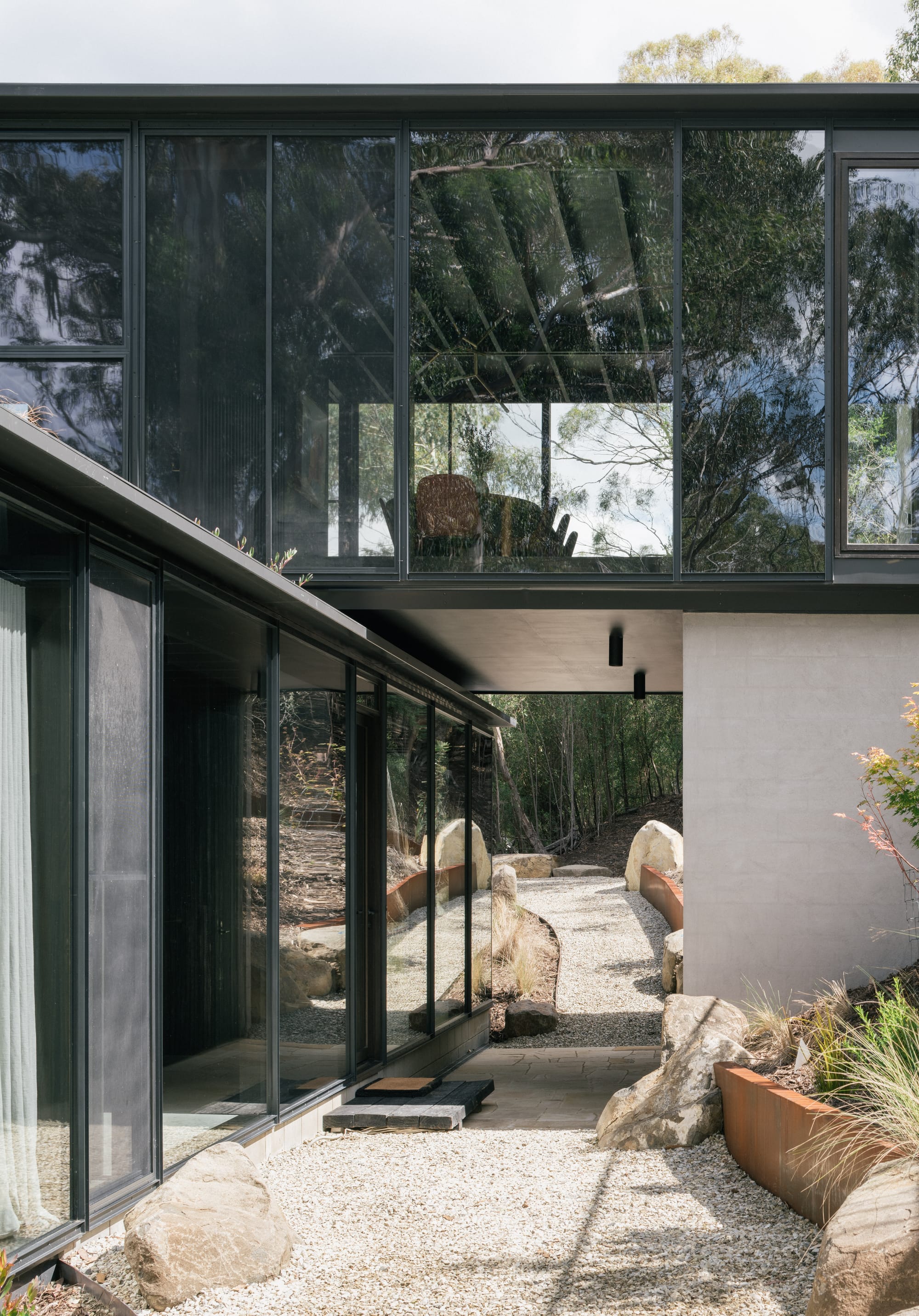 Taroona House by Archier. Photography by Thurston Empson. Two rectangular structures stacked on top of one another. Rendered brick, glass and black. Stone pathway through buildings. 