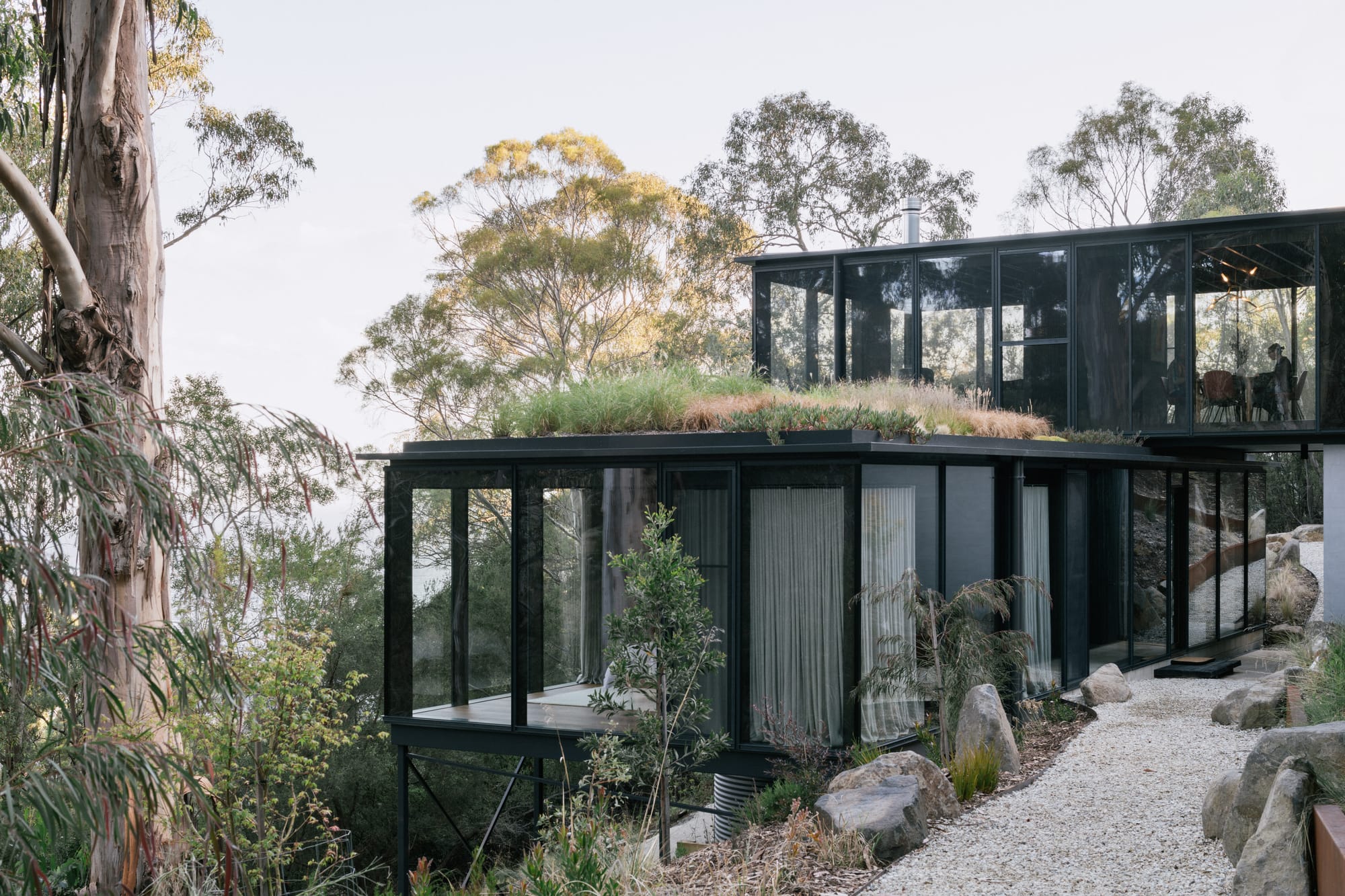 Taroona House by Archier. Photography by Thurston Empson. Stacked, multistory glass and black home. Hanging off hill in bush. 