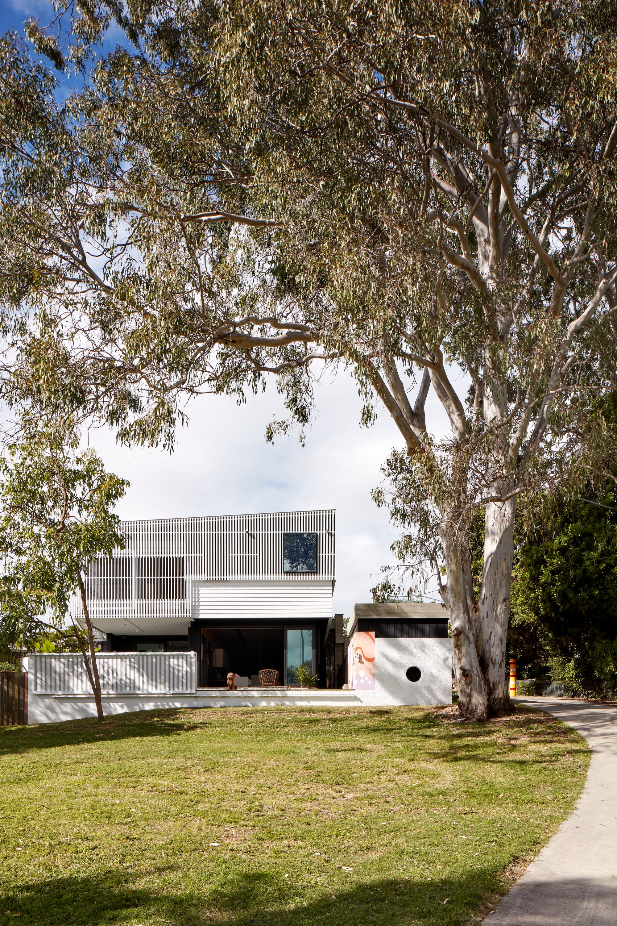Uxbridge House by Tim Stewart Architects. Photography by Christopher Frederick Jones. Exterior of double storey home with large opening between inside and out. Large grass area at front of house with path to right.