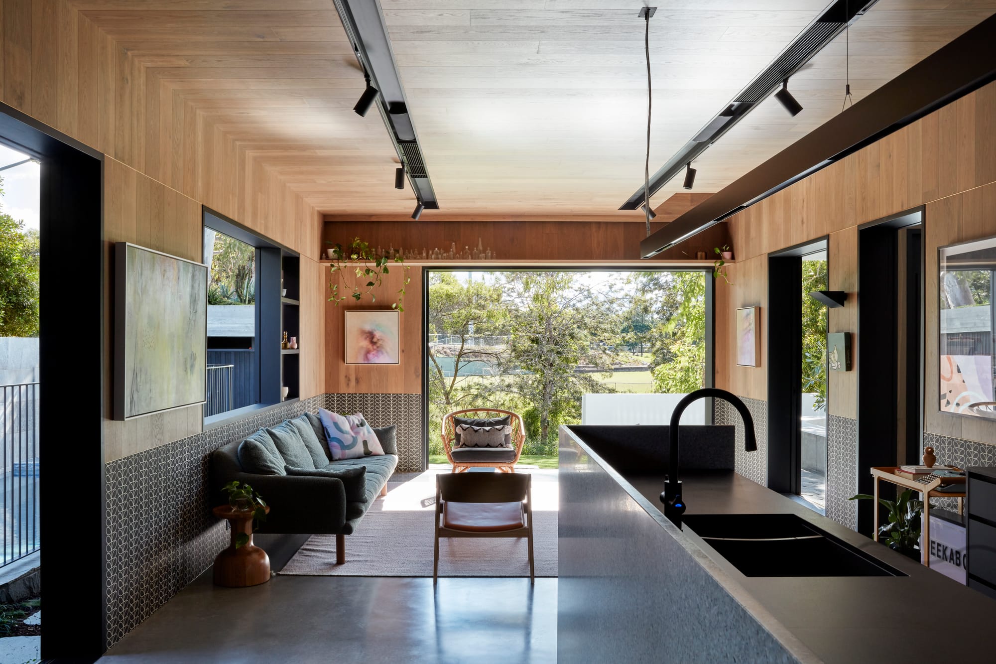 Uxbridge House by Tim Stewart Architects. Photography by Christopher Frederick Jones. Open plan kitchen and living space with timber walls and ceiling. Large door on back wall opening onto garden and views of park. 