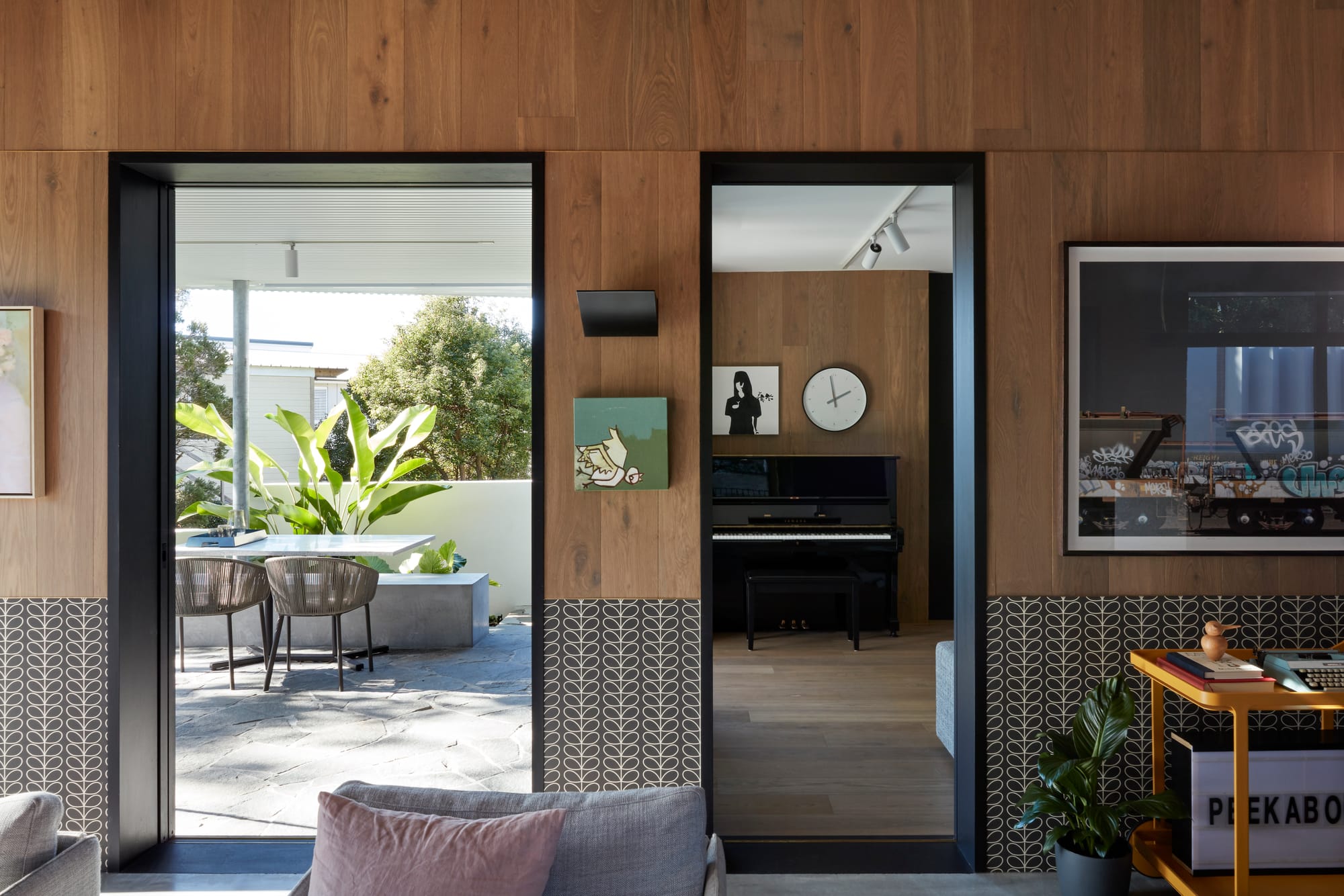 Uxbridge House by Tim Stewart Architects. Photography by Christopher Frederick Jones. Interior of home with wood panelled walls. One door leading to room with a black piano and one door leading to courtyard.