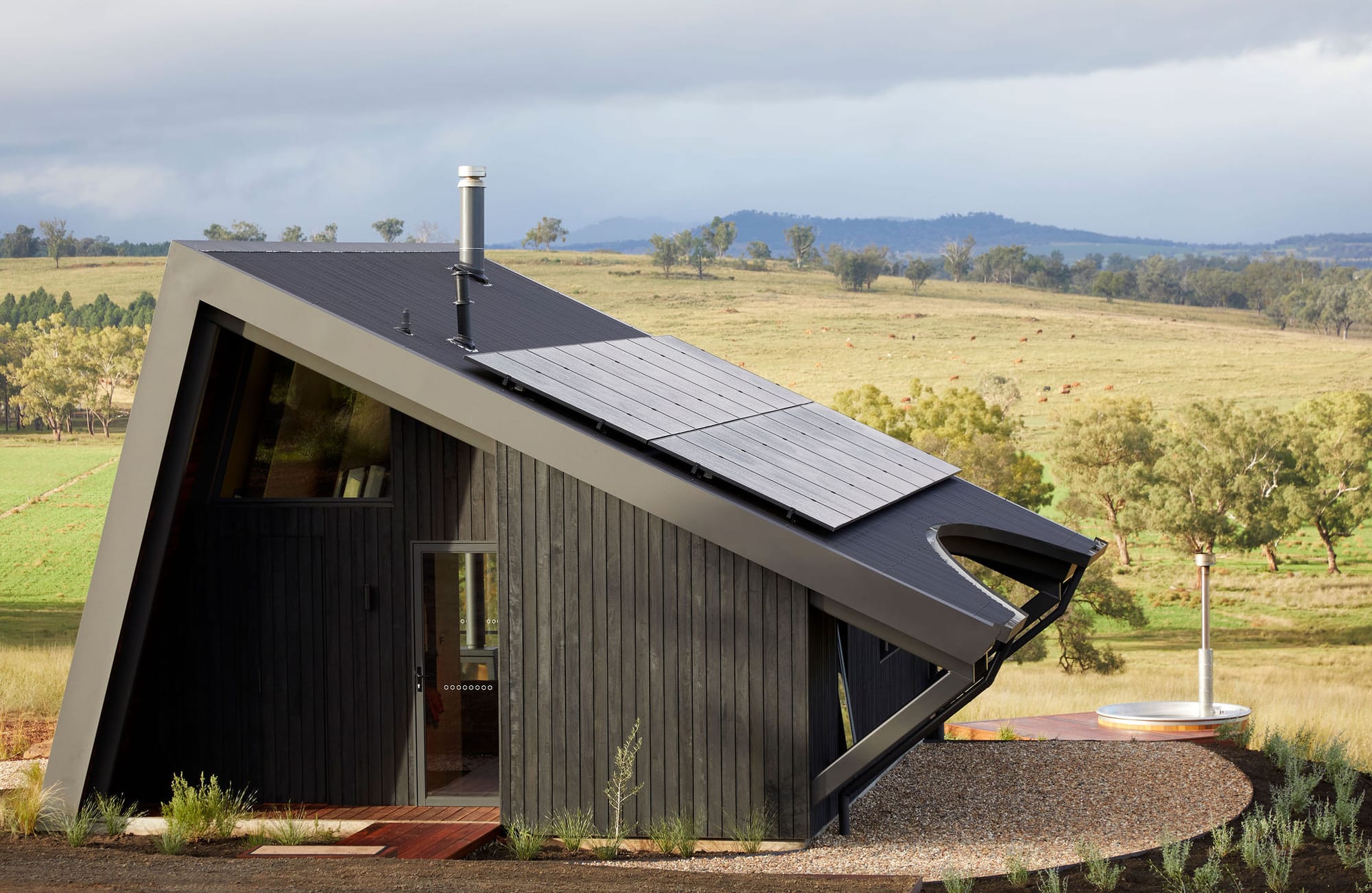An exterior shot of Gilay Estate showing the entry to the cabin with black cladding and rooftop solar with the hinterland view in the background